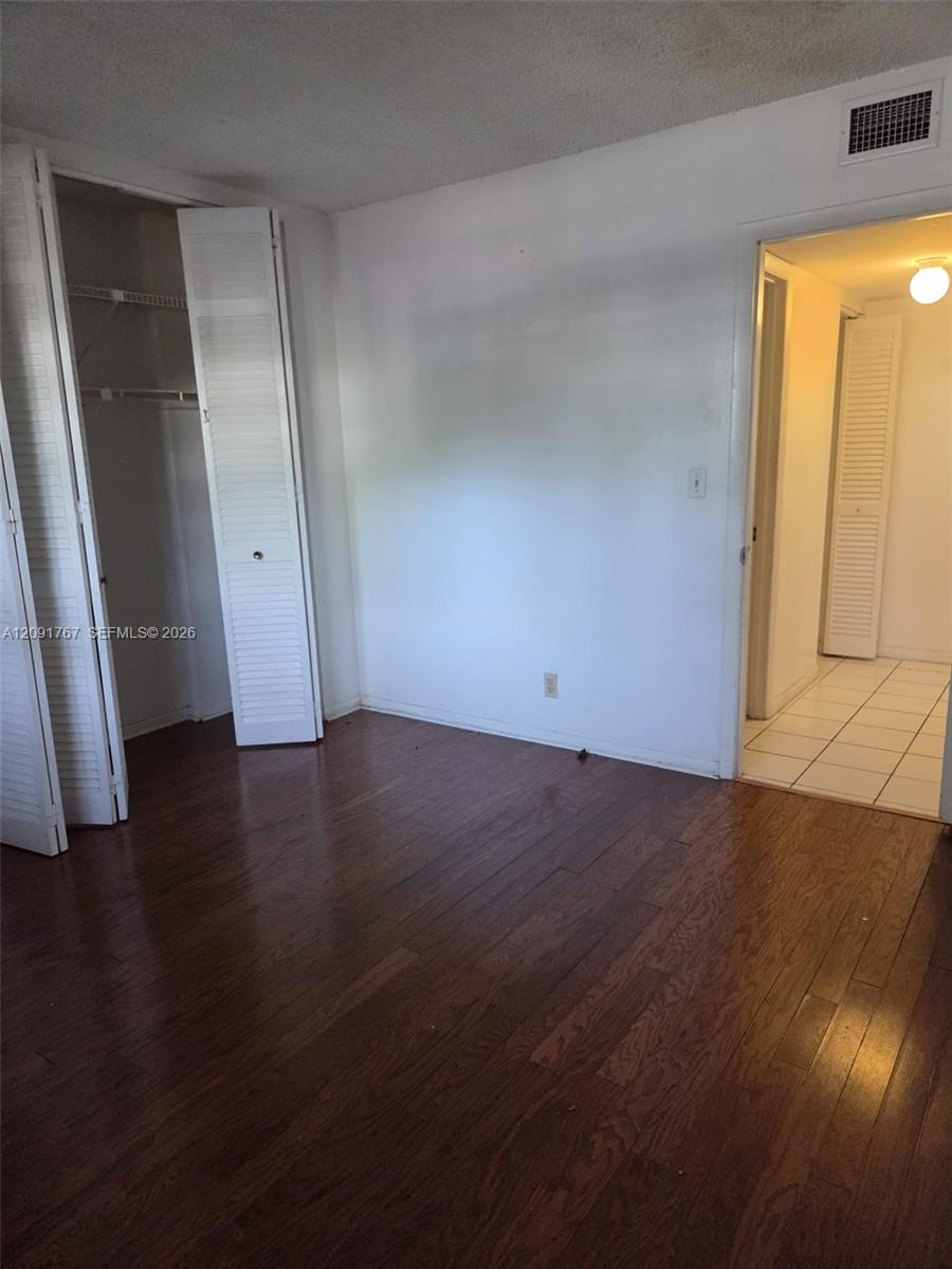 Room featuring dark wood-finish flooring, a built-in closet with louvered bifold doors, and a doorway opening to a tiled area Room featuring dark wood-finish flooring, a built-in closet with louvered bifold doors, and a doorway opening to a tiled area