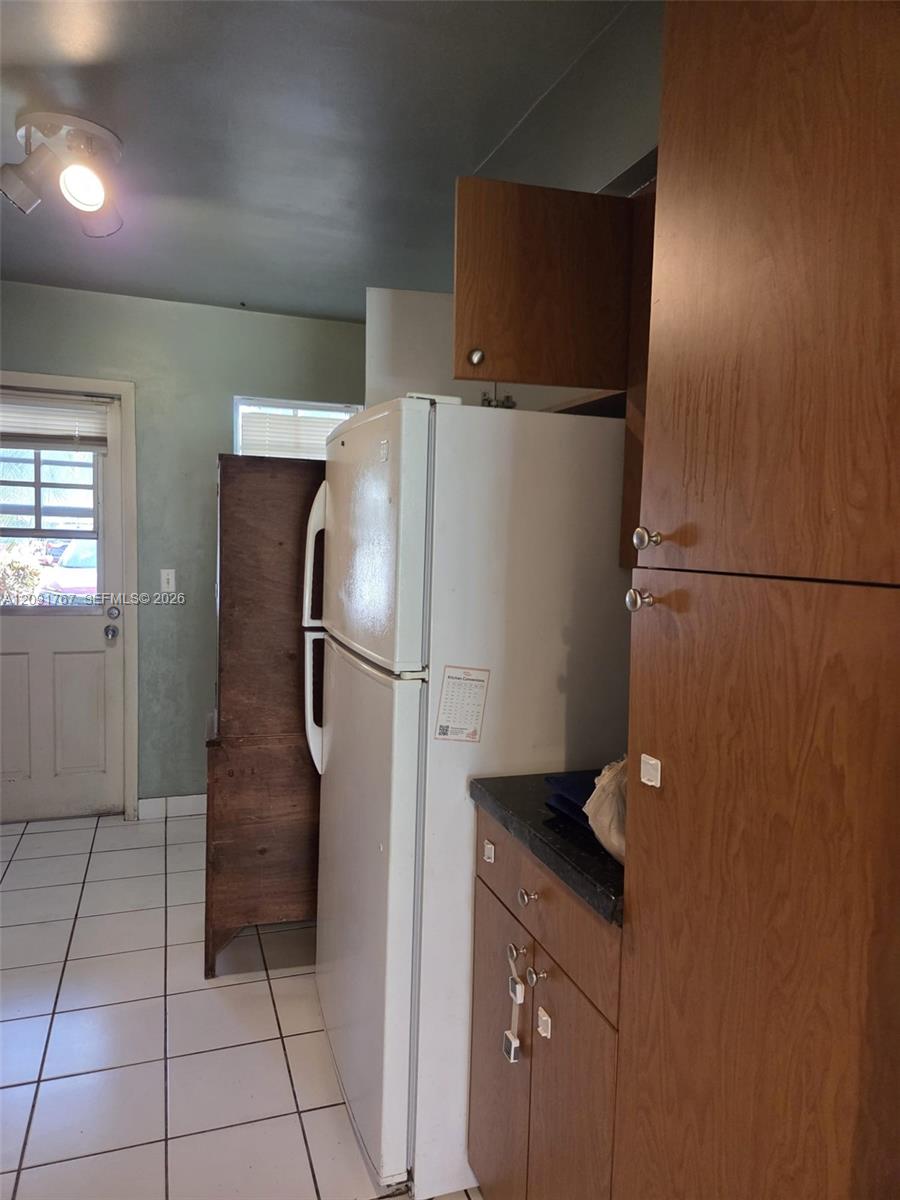 Wood-finish cabinetry, floor-to-ceiling pantry storage, ceramic tile flooring, and multi-light ceiling fixture Wood-finish cabinetry, floor-to-ceiling pantry storage, ceramic tile flooring, and multi-light ceiling fixture