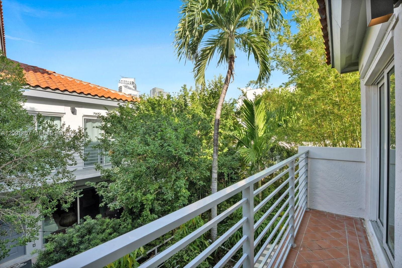 Outdoor balcony featuring red tile flooring, horizontal metal railings, and mature palm tree landscaping