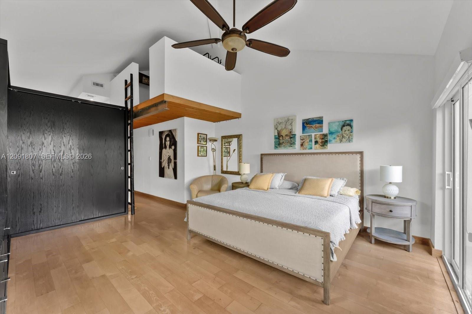 Vaulted ceilings featuring a prominent ceiling fan, wood-finish flooring, floor-to-ceiling dark-finish cabinetry, a built-in ladder, and sliding glass doors