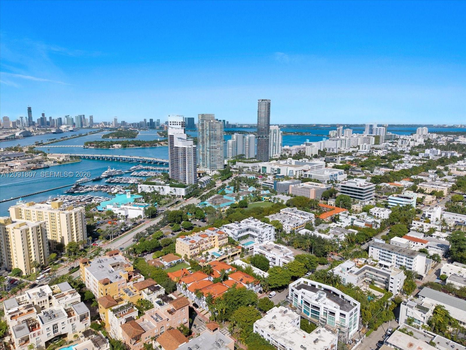 Aerial perspective of urban landscape featuring waterfront exposure, high-rise buildings, marina, bridges, and expansive coastal horizon