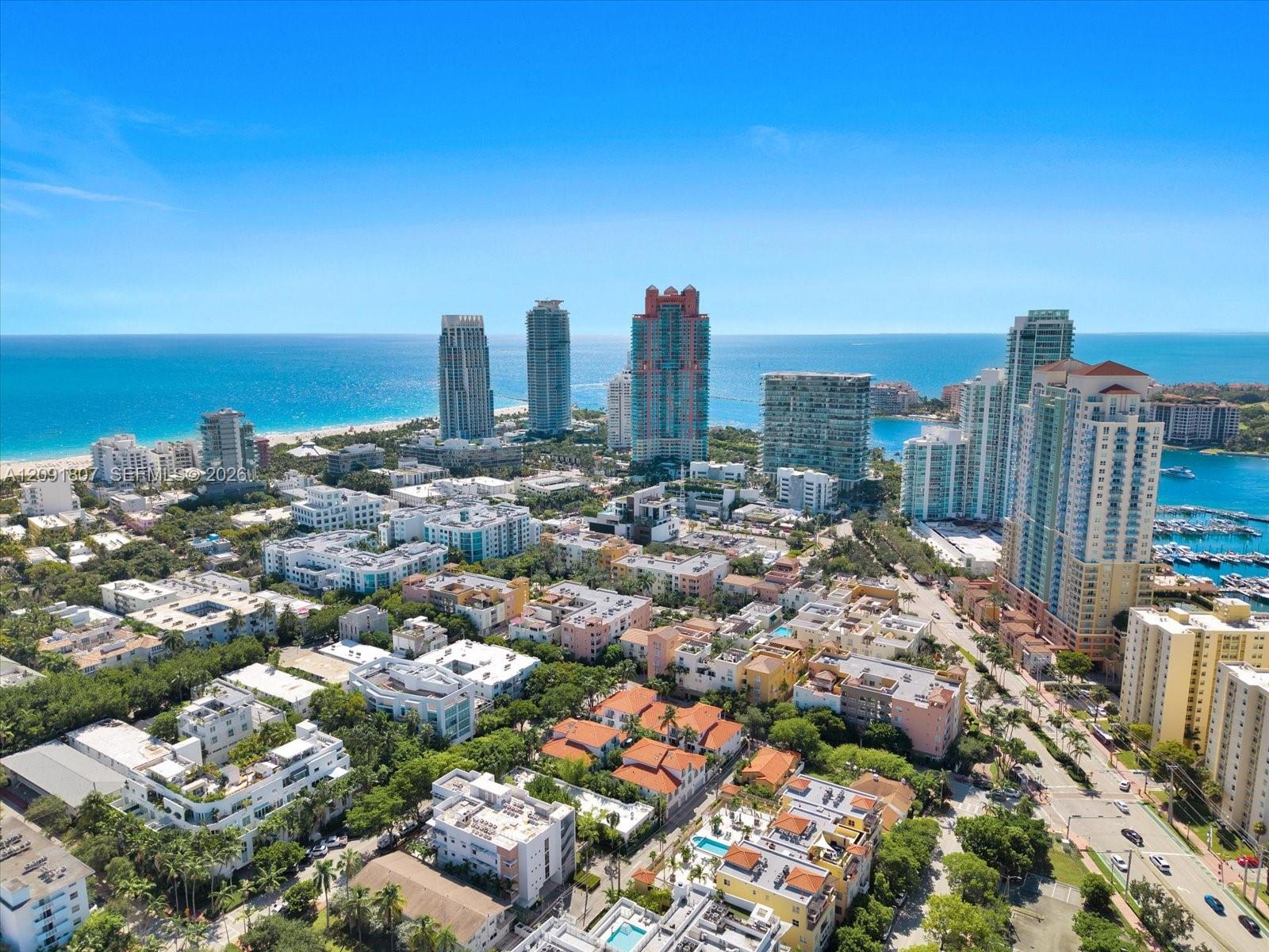 Aerial perspective of a coastal urban landscape featuring high-rise towers, proximity to the shoreline, a marina, and dense metropolitan infrastructure