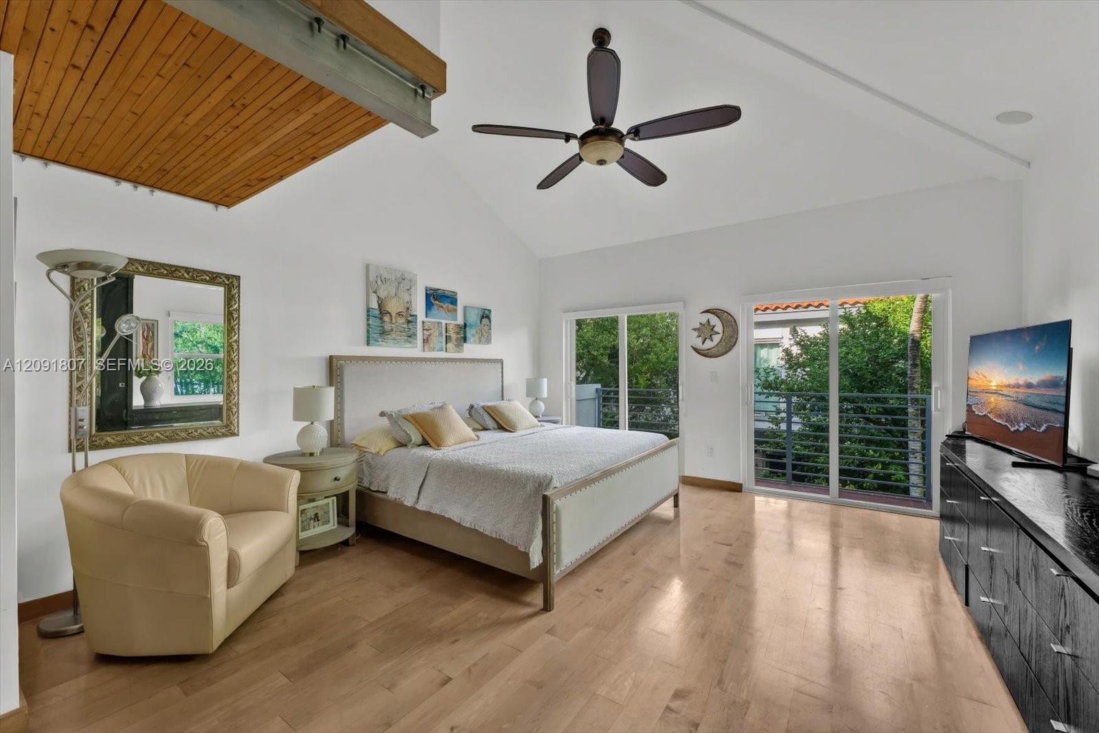 Vaulted ceilings with wood-plank detailing, wood-finish flooring, and sliding glass doors with balcony access