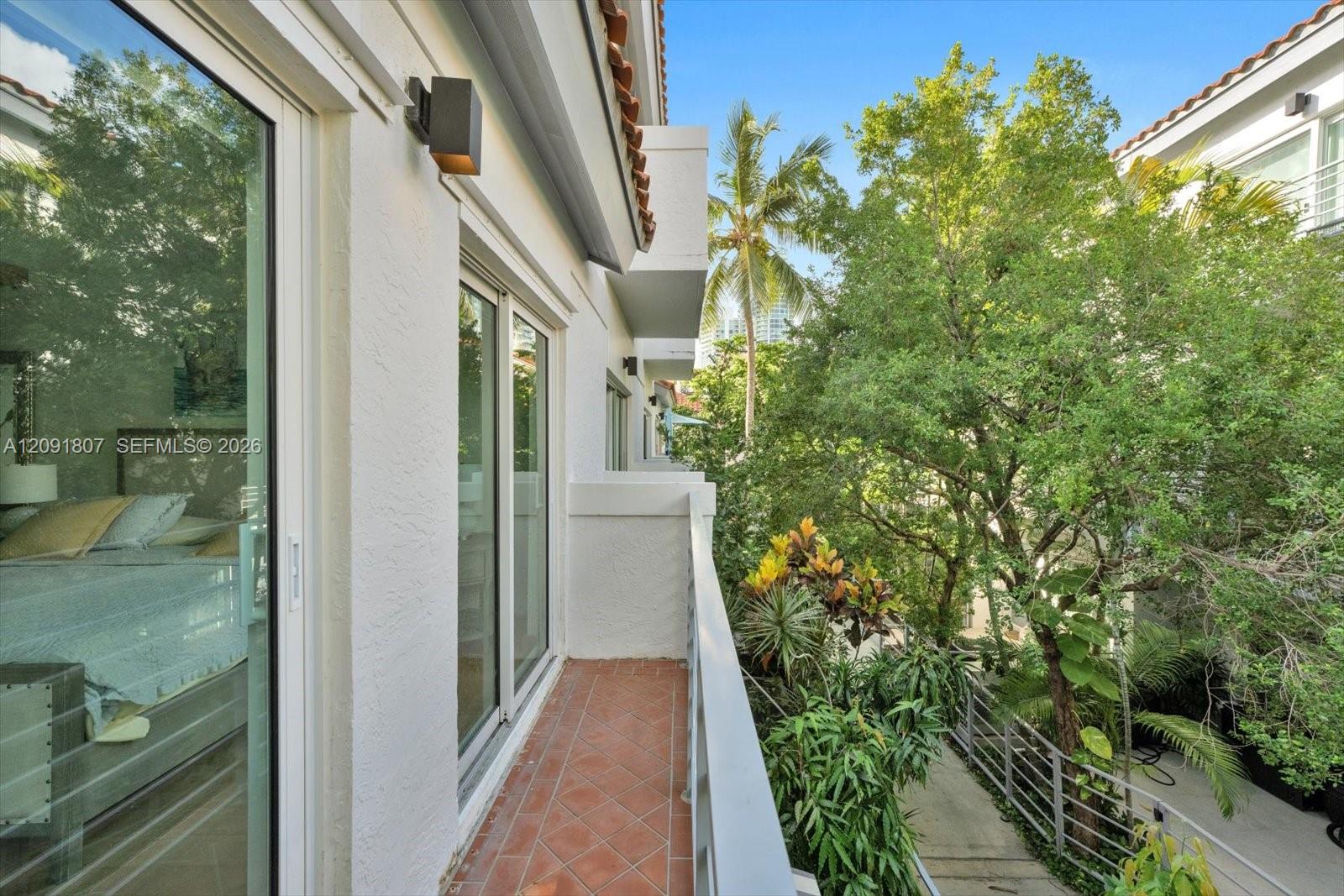 Exterior balcony featuring terracotta tile flooring, metal railing, stucco wall finish, and wall-mounted exterior lighting
