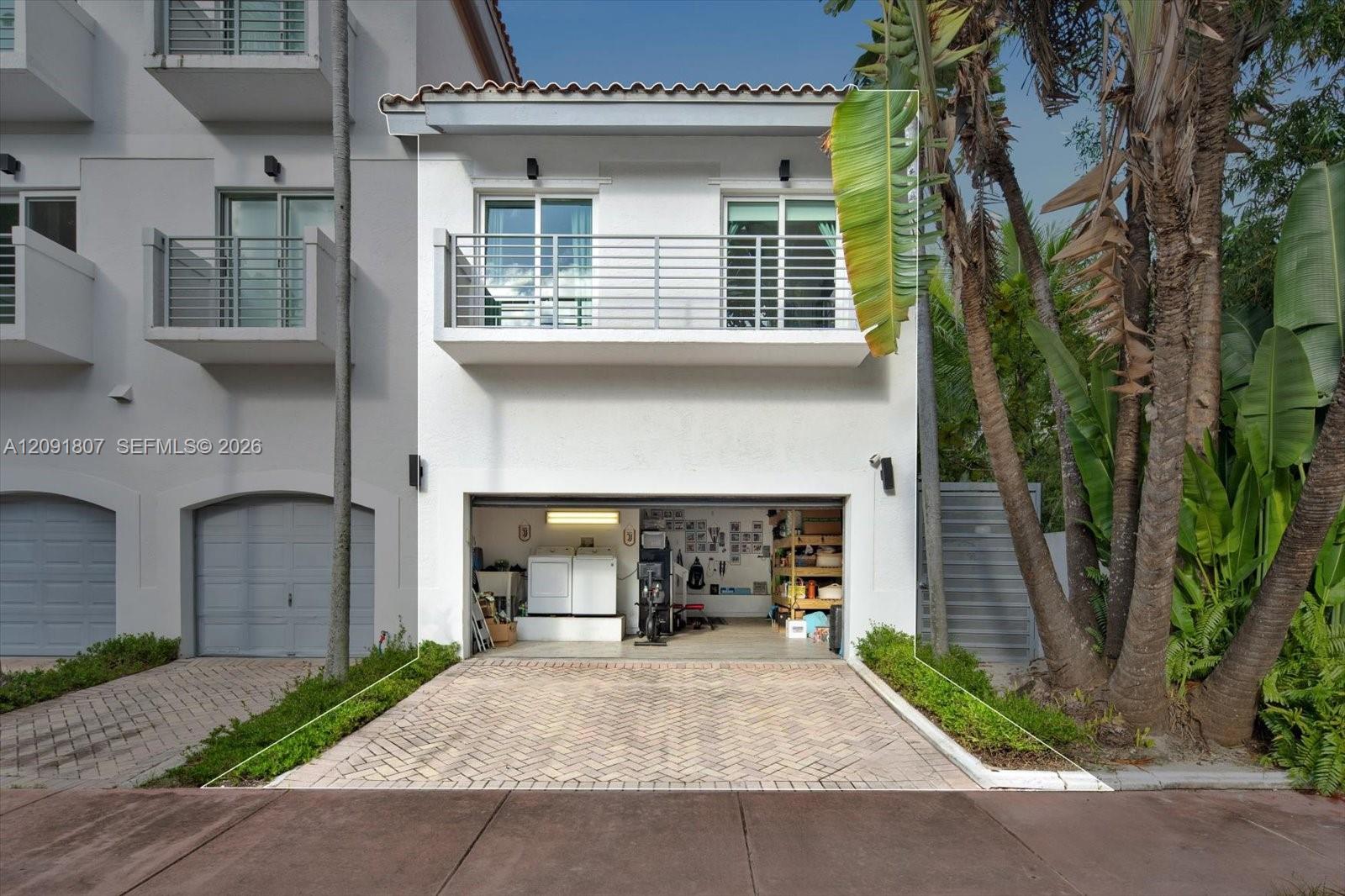 Stucco exterior featuring a second-story balcony with metal railing, a paved driveway, and an attached multi-purpose garage