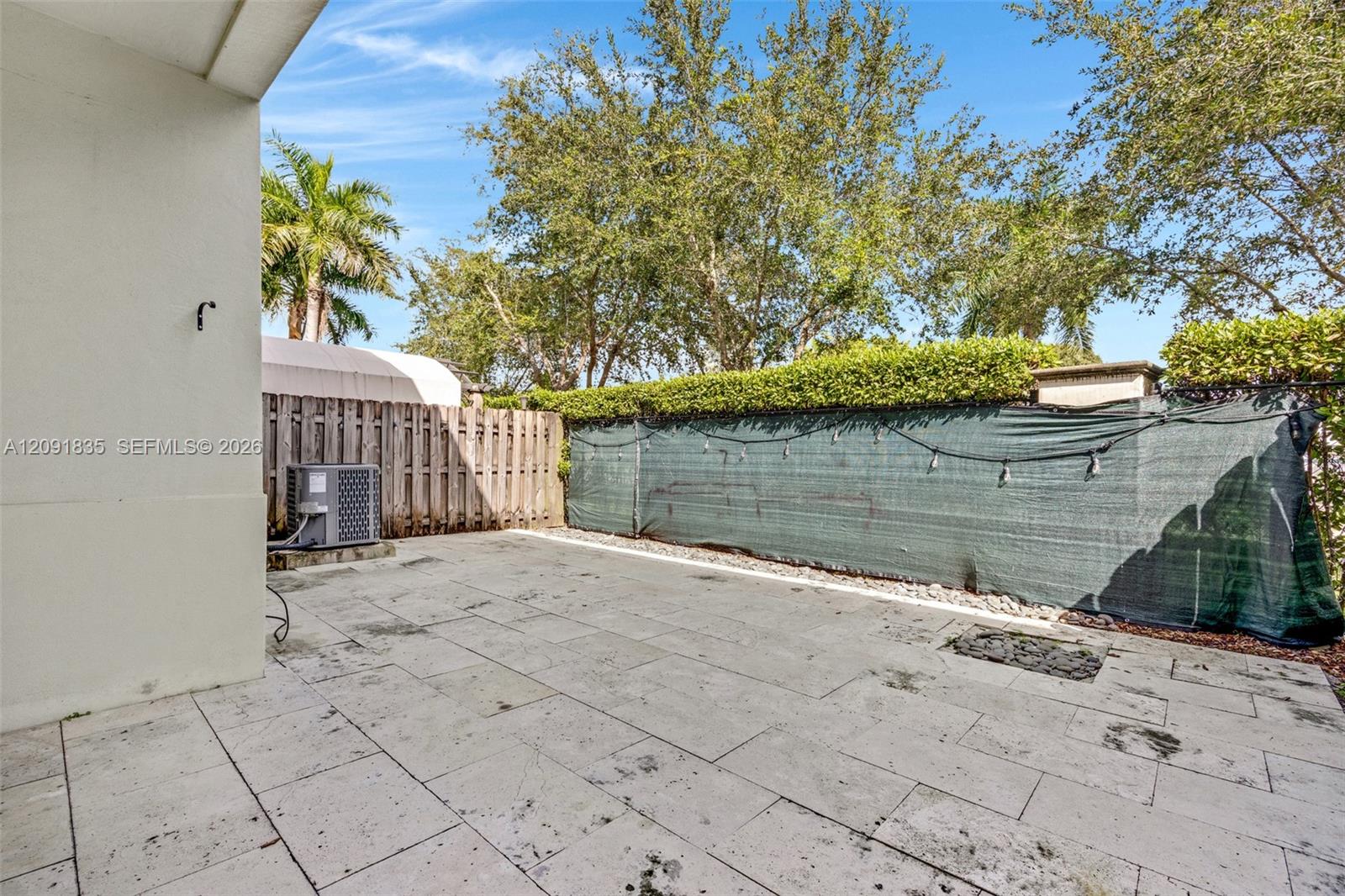 Concrete paver patio with a smooth-finish exterior wall, privacy fencing, and mature trees