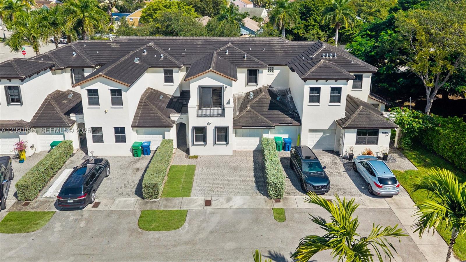 Multi-unit structure featuring a light-toned stucco exterior, dark shingle roof, paved private driveways, and upper-level balconies