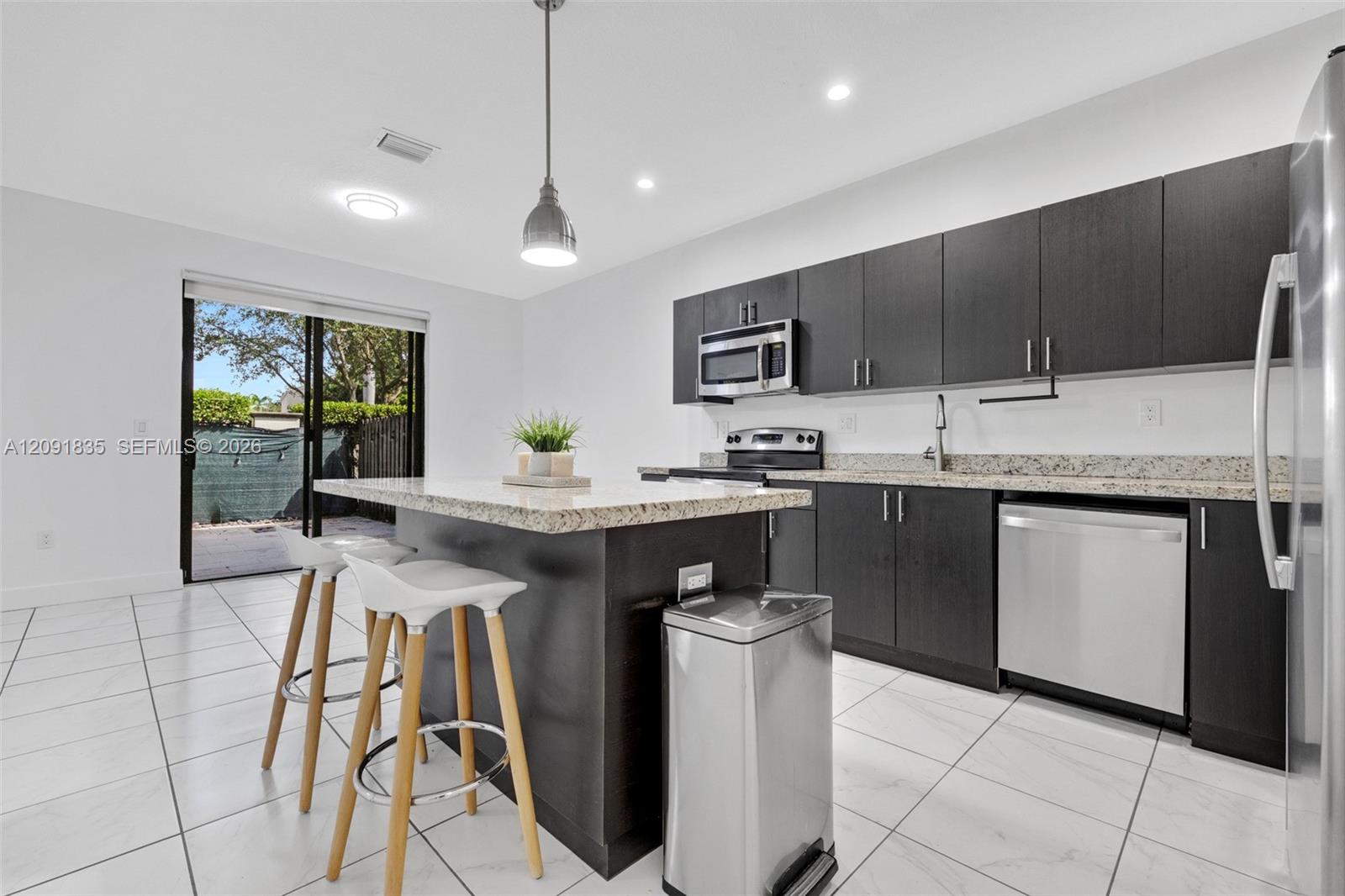 Kitchen featuring dark-toned flat-panel cabinetry, stone countertops, stainless steel appliances, a center island, and large-format tile flooring