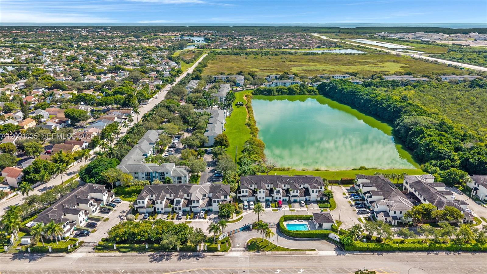 Aerial perspective of a multi-unit residential community featuring a dedicated swimming pool, paved parking, and direct frontage on a natural lake