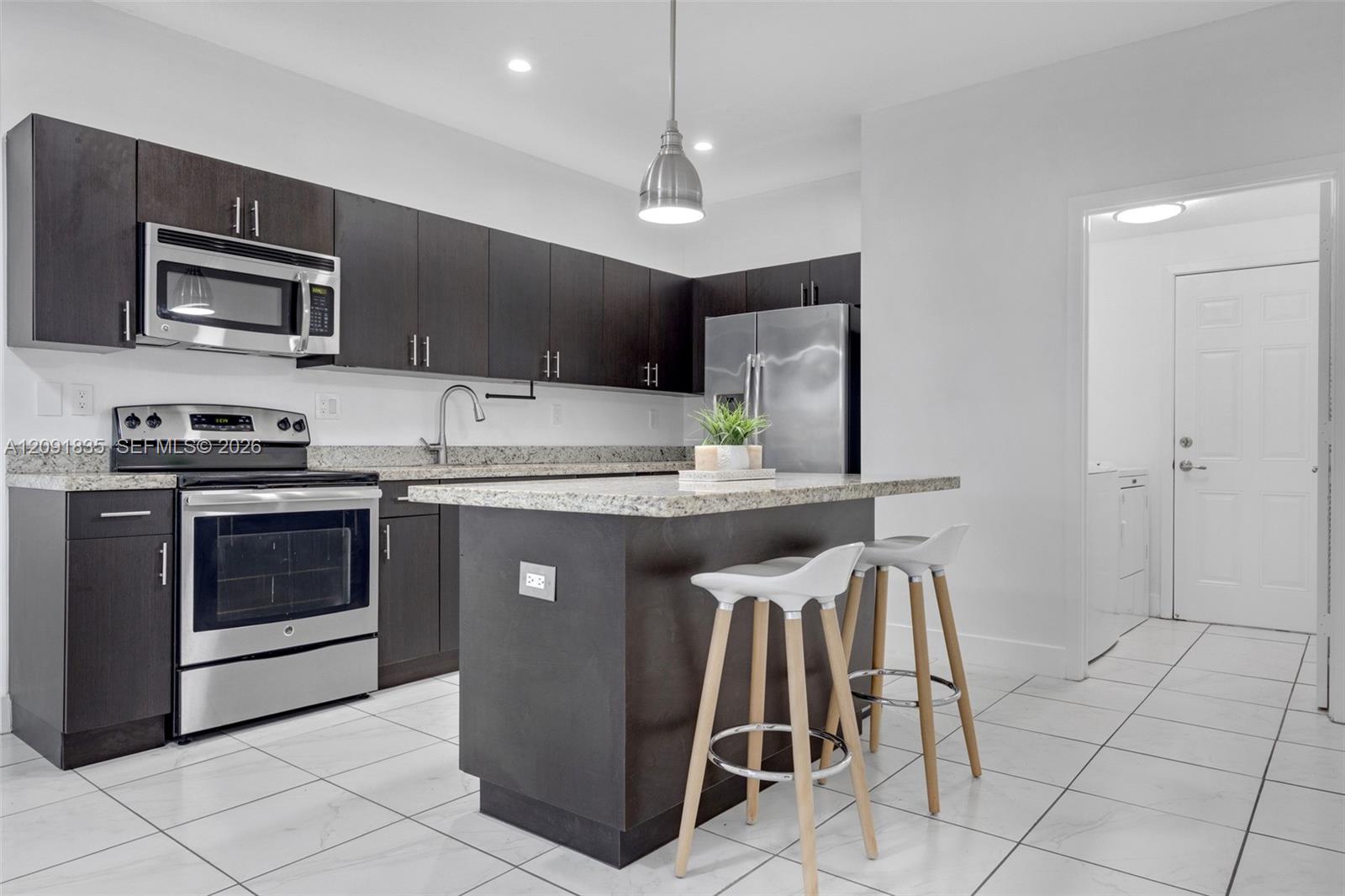 Kitchen featuring dark-finish cabinetry, stone-style countertops, stainless steel appliances, a central island, and ceramic tile flooring