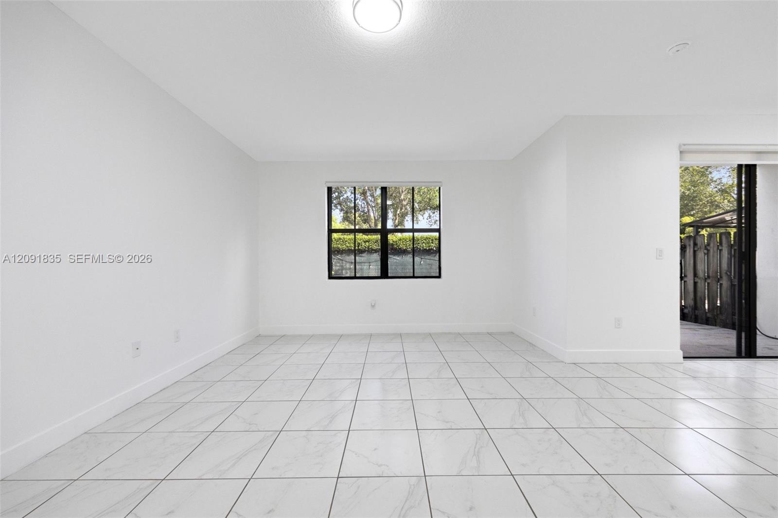 Interior space featuring large-format tile flooring, a centered window with black-framed panes, neutral walls, and sliding glass patio doors