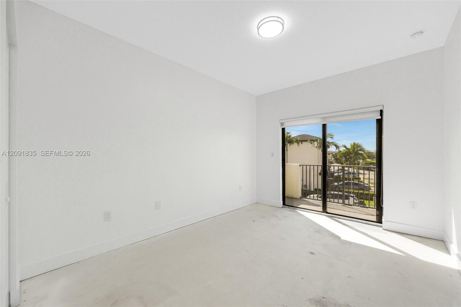 Interior space featuring neutral wall paint, flush-mount ceiling lighting, and sliding glass doors opening to a balcony with metal railings
