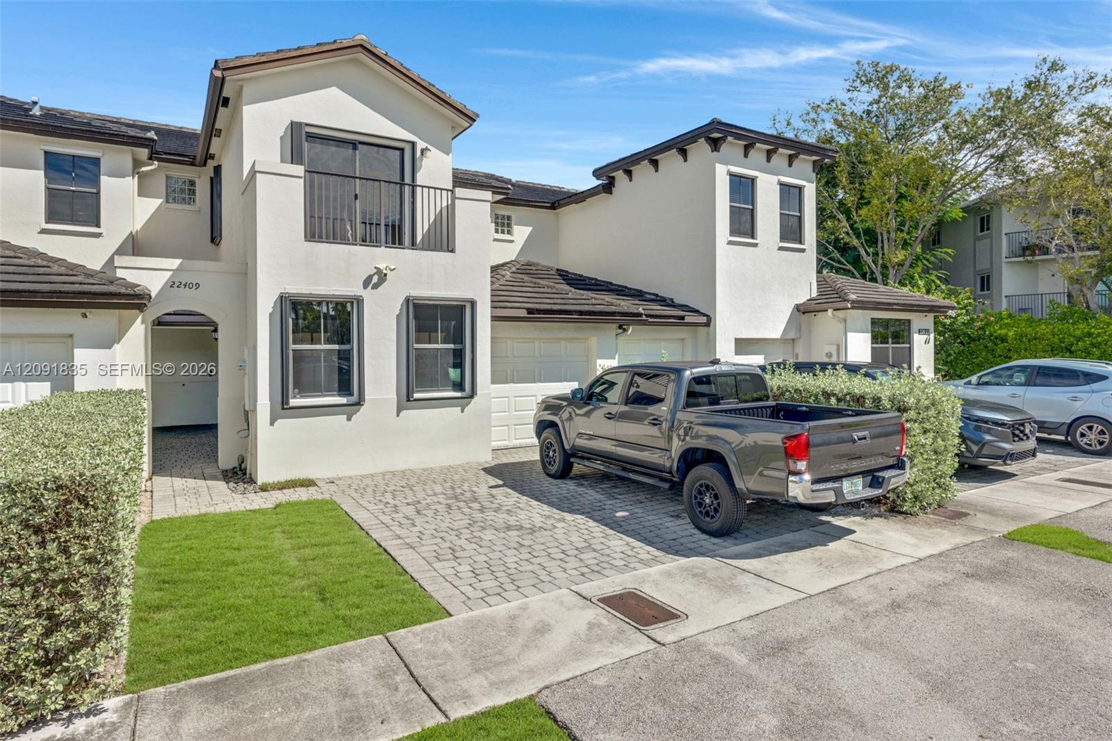 Two-story stucco exterior featuring a tiled roof, upper-level balcony with metal railing, paver driveway, and an integrated garage