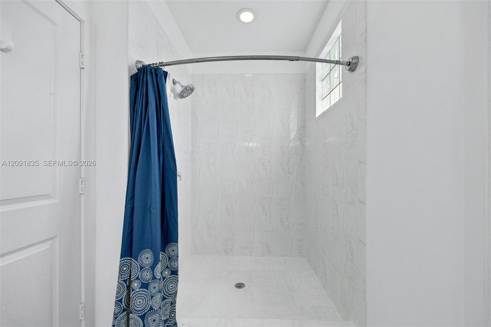 Walk-in shower featuring white stone-finish wall tile, recessed ceiling lighting, a fixed shower head, and a glass block window