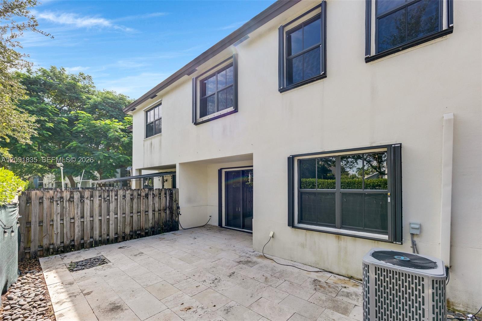 Stucco exterior featuring a paved stone patio, sliding glass doors, and a wood privacy fence