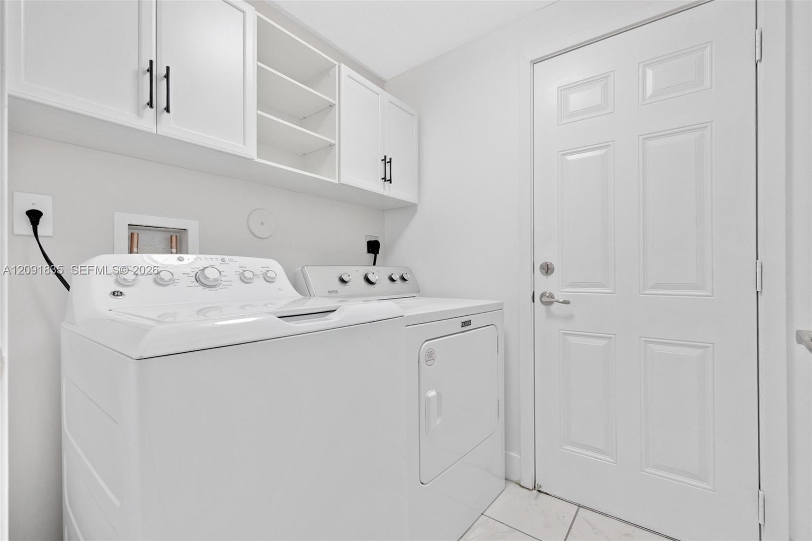 Laundry area featuring white shaker-style wall cabinets with matte black hardware, open shelving, and tile flooring