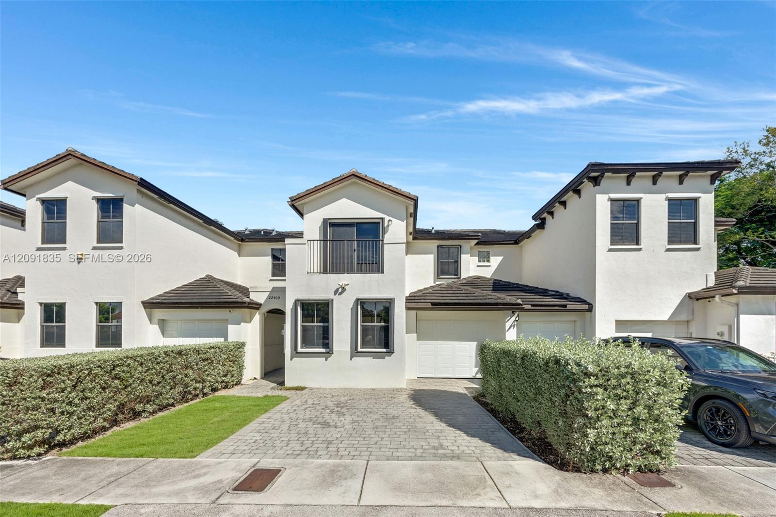 Stucco exterior featuring multiple attached garage bays, a paved driveway, and an upper-level balcony with metal railings Stucco exterior featuring multiple attached garage bays, a paved driveway, and an upper-level balcony with metal railings