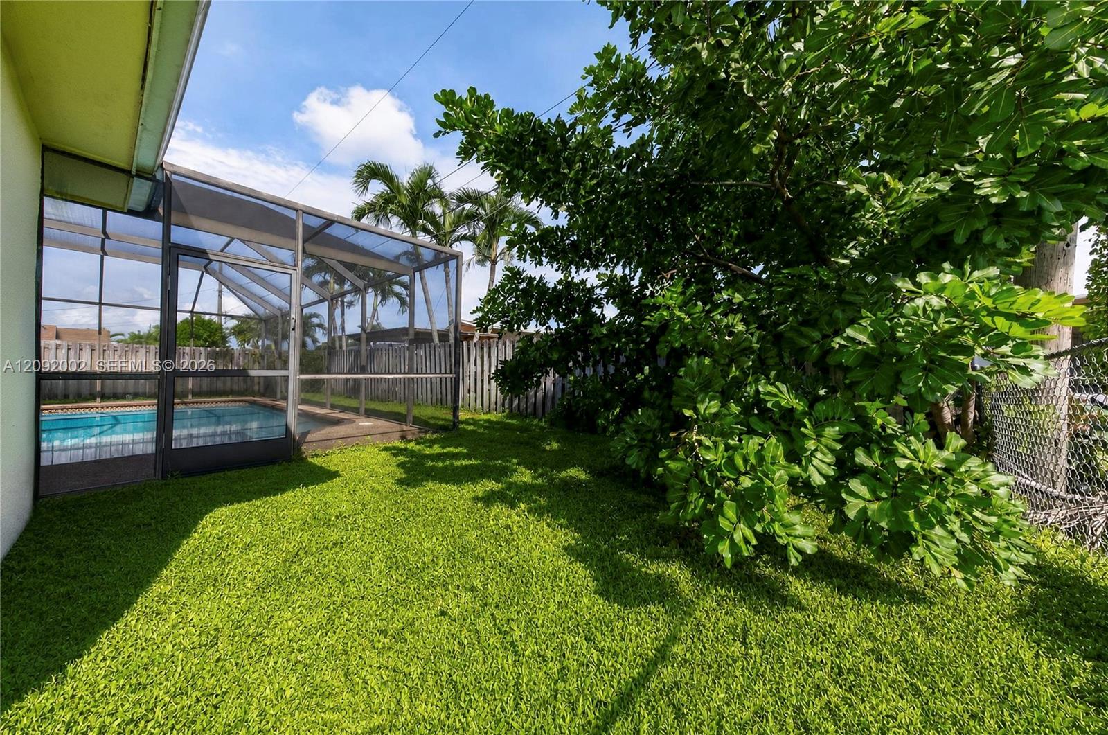 Screen-enclosed swimming pool featuring a concrete deck and fenced backyard with mature trees