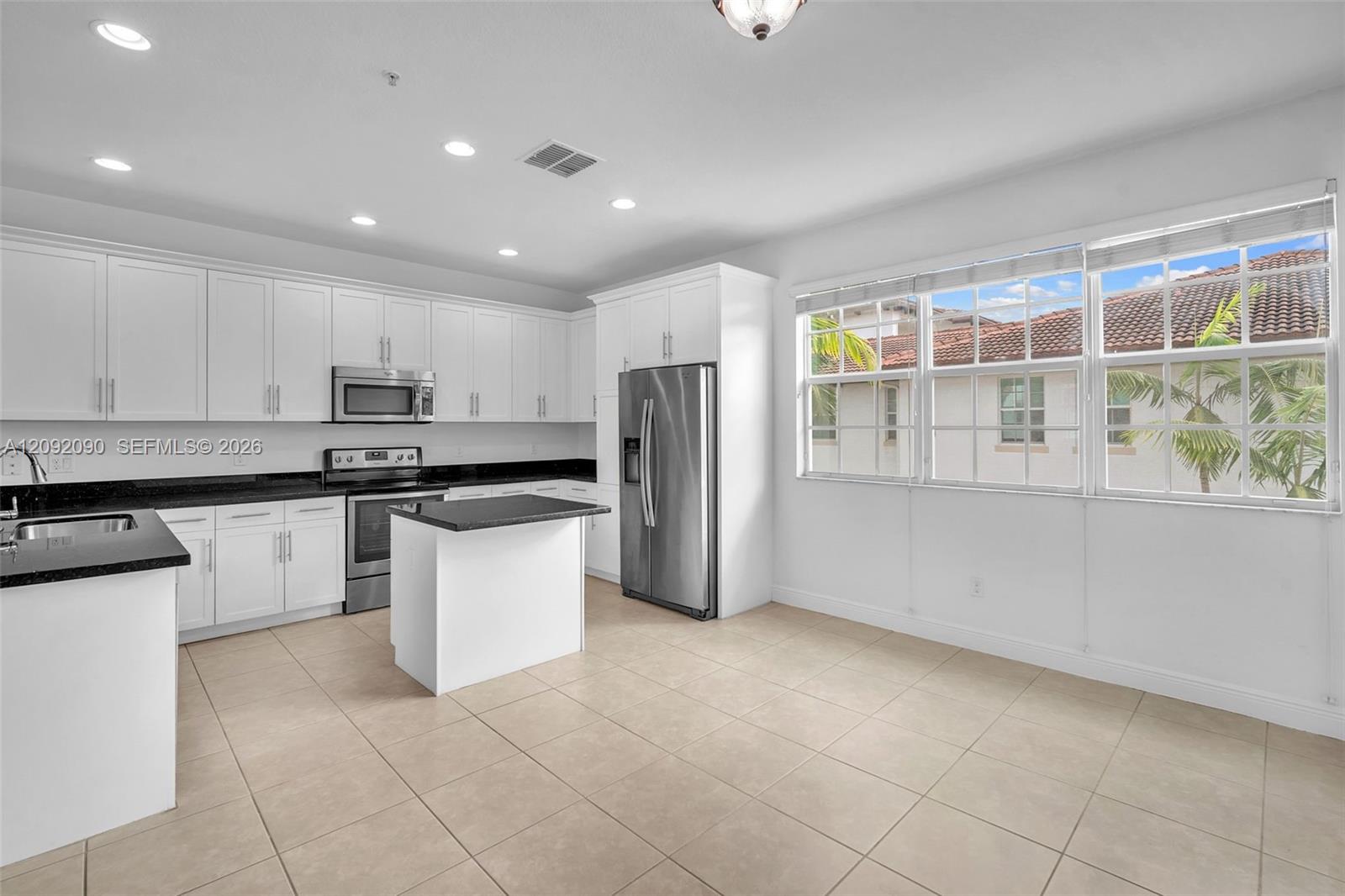 Kitchen featuring white cabinetry, dark stone countertops, stainless steel appliances, a center island, and large windows with integrated blinds
