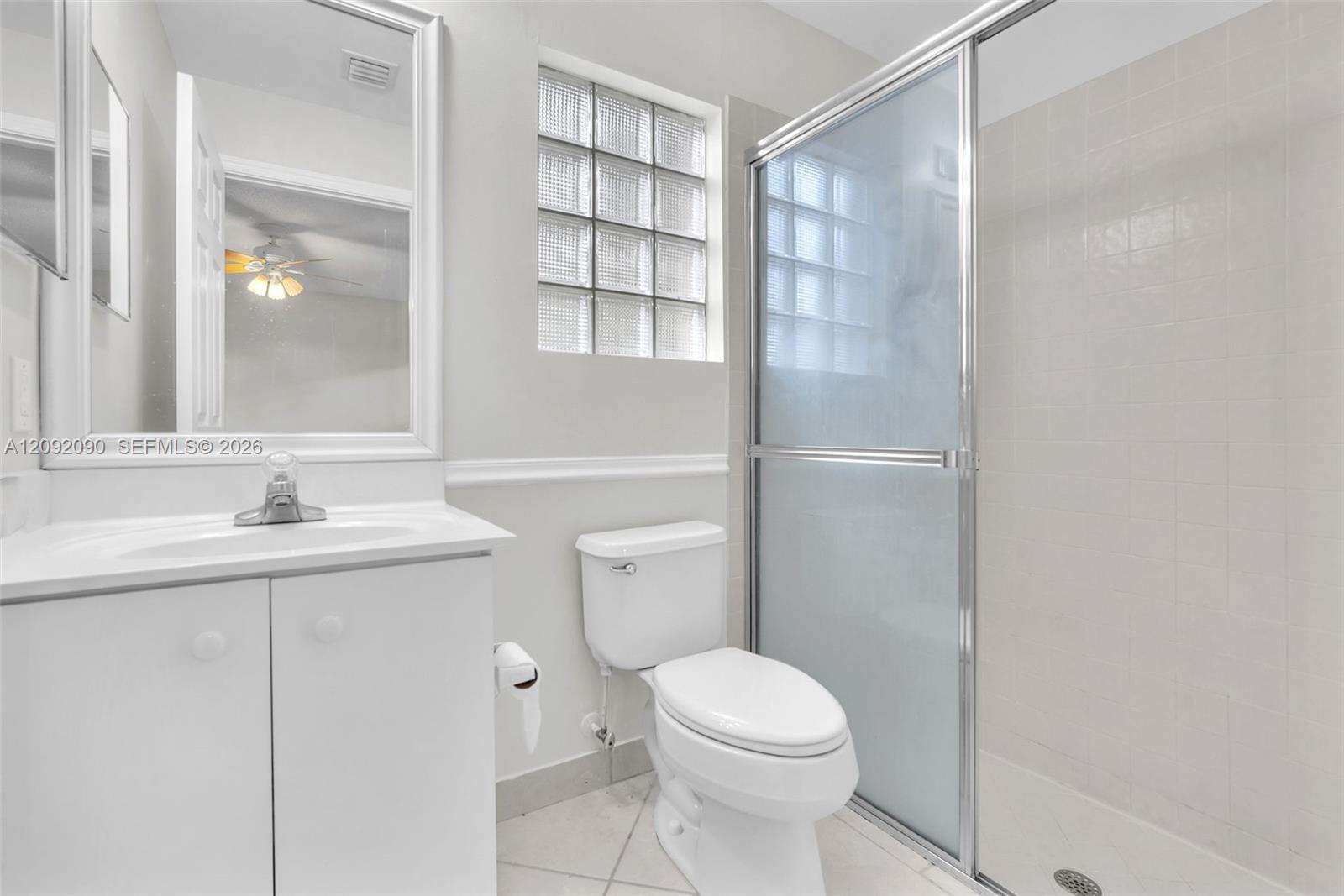 Bathroom featuring a vanity with an integrated sink, glass block window, walk-in shower with a sliding enclosure, and ceramic tile flooring