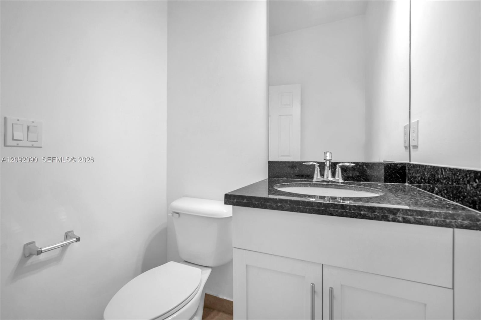 Vanity featuring a dark stone countertop, integrated oval basin, white shaker-style cabinetry, and polished chrome hardware, complemented by a large wall-mounted mirror