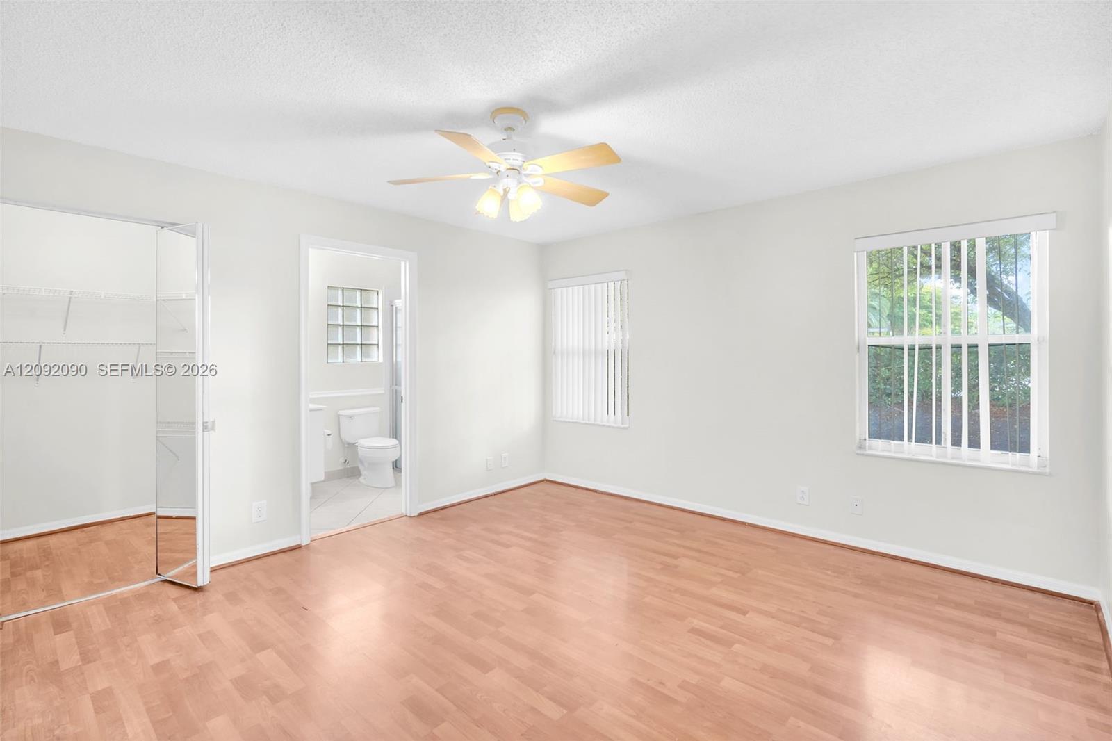 Room featuring wood-finish flooring, a ceiling fan with integrated lighting, dual windows with vertical blinds, and a built-in walk-in closet with mirrored door panels