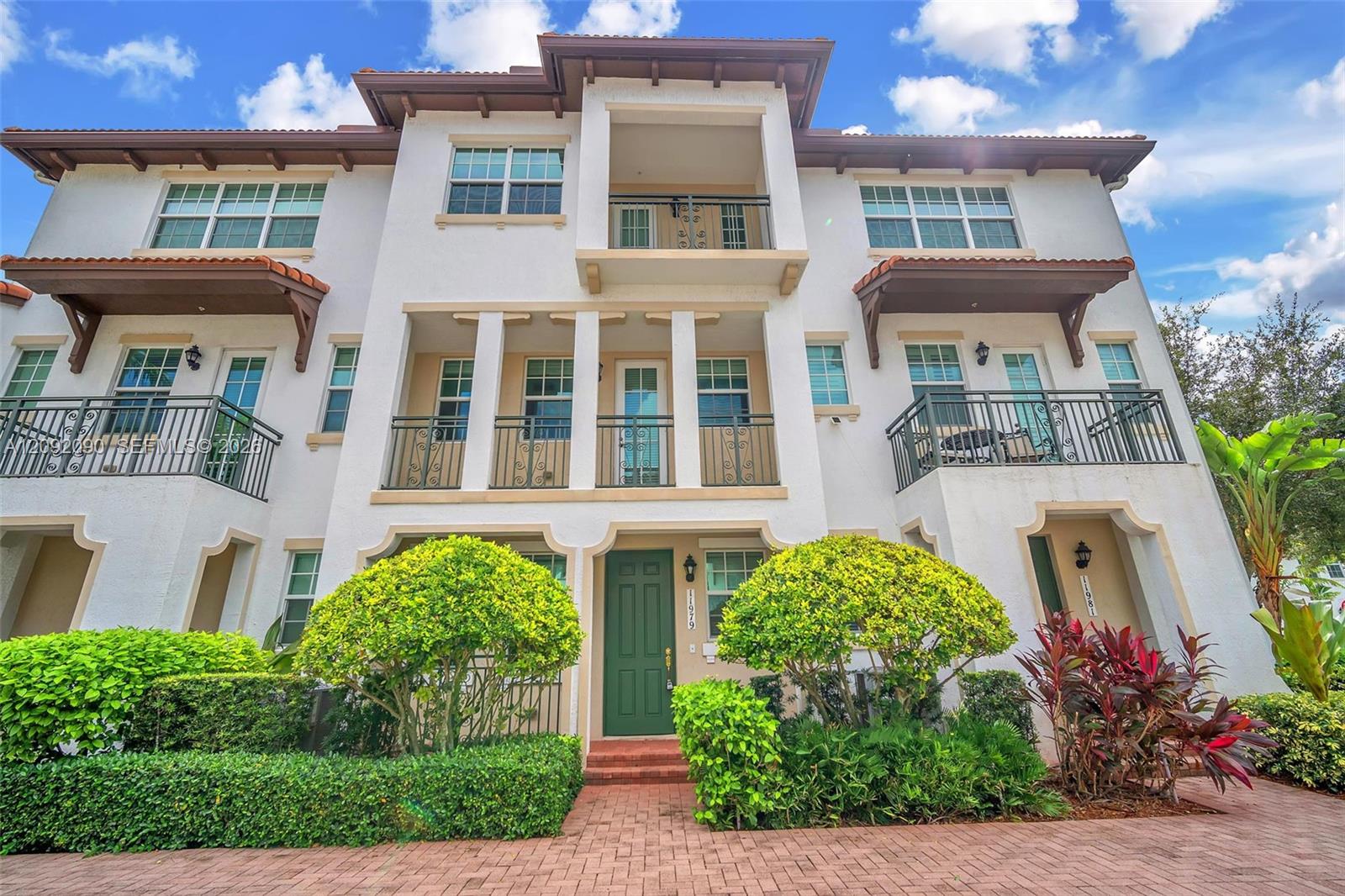 Stucco multi-story exterior featuring a tile roof, multiple wrought-iron balconies, arched entryway detailing, and brick-paver hardscaping