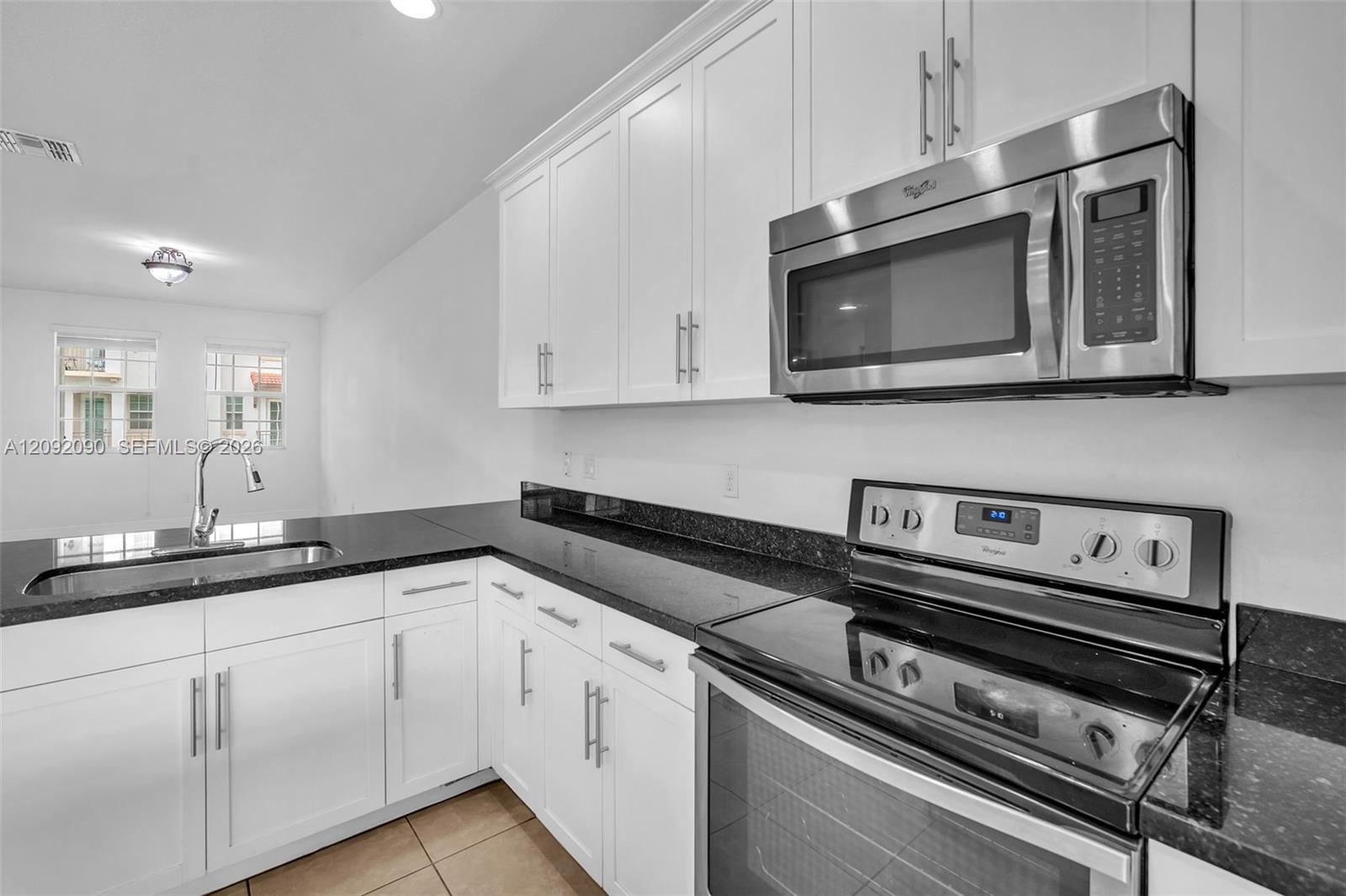Kitchen featuring white shaker-style cabinetry, dark stone countertops, stainless steel appliances, and an undermount sink with a high-arch pull-down faucet