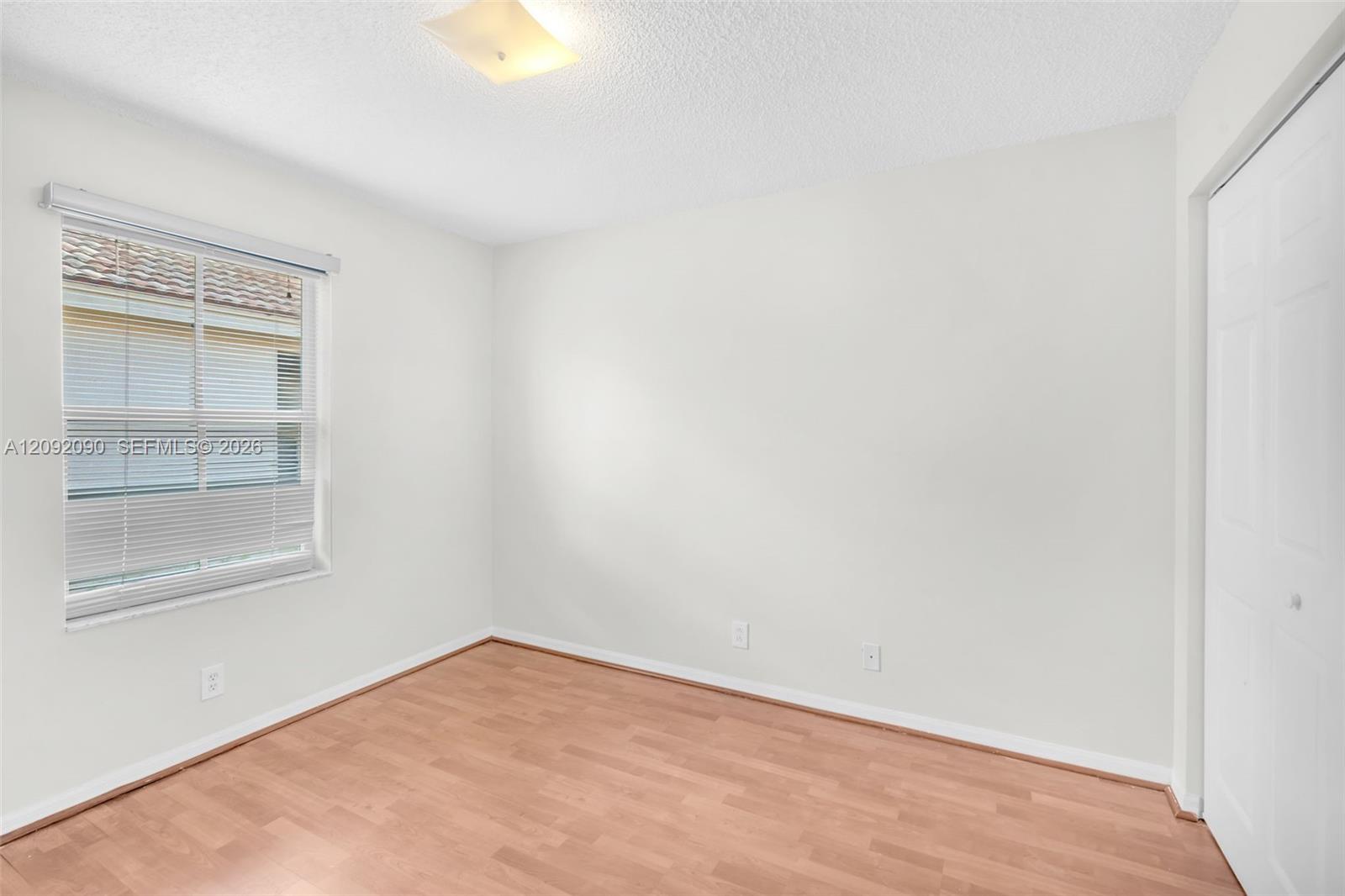 Room featuring wood-finish flooring, a neutral color palette, a window with horizontal blinds, and a built-in closet with double doors