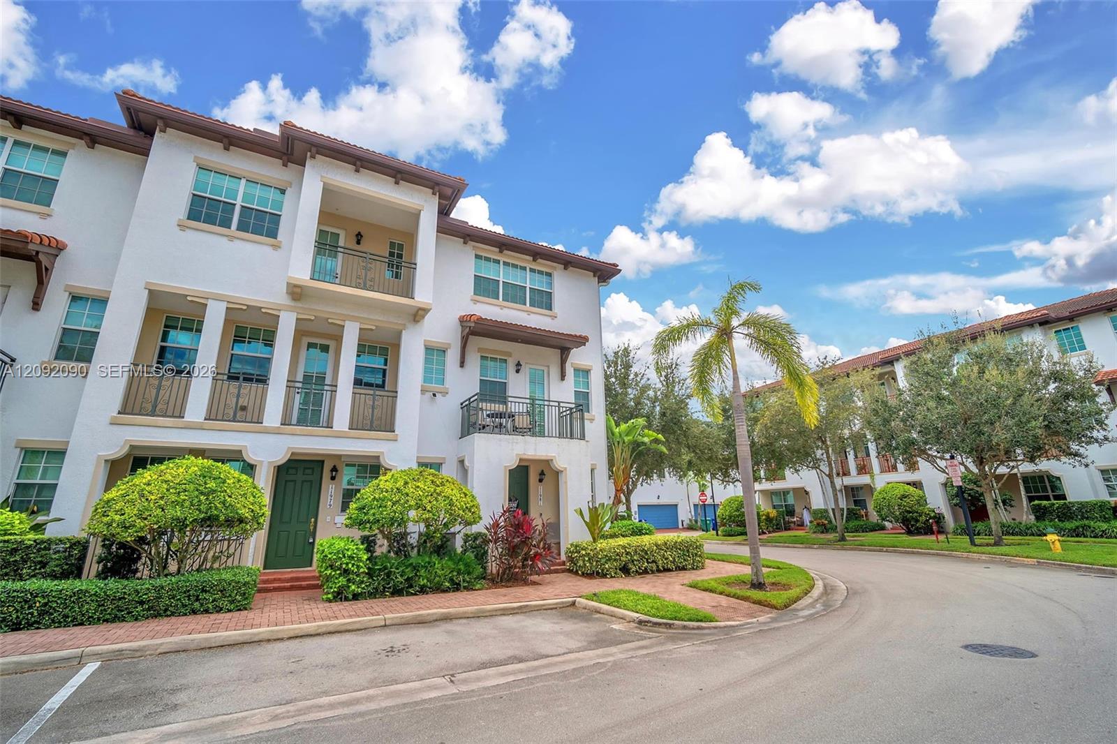 Stucco exterior featuring multi-level balconies with wrought-iron railings, arched entryway detailing, and brick-paver walkway