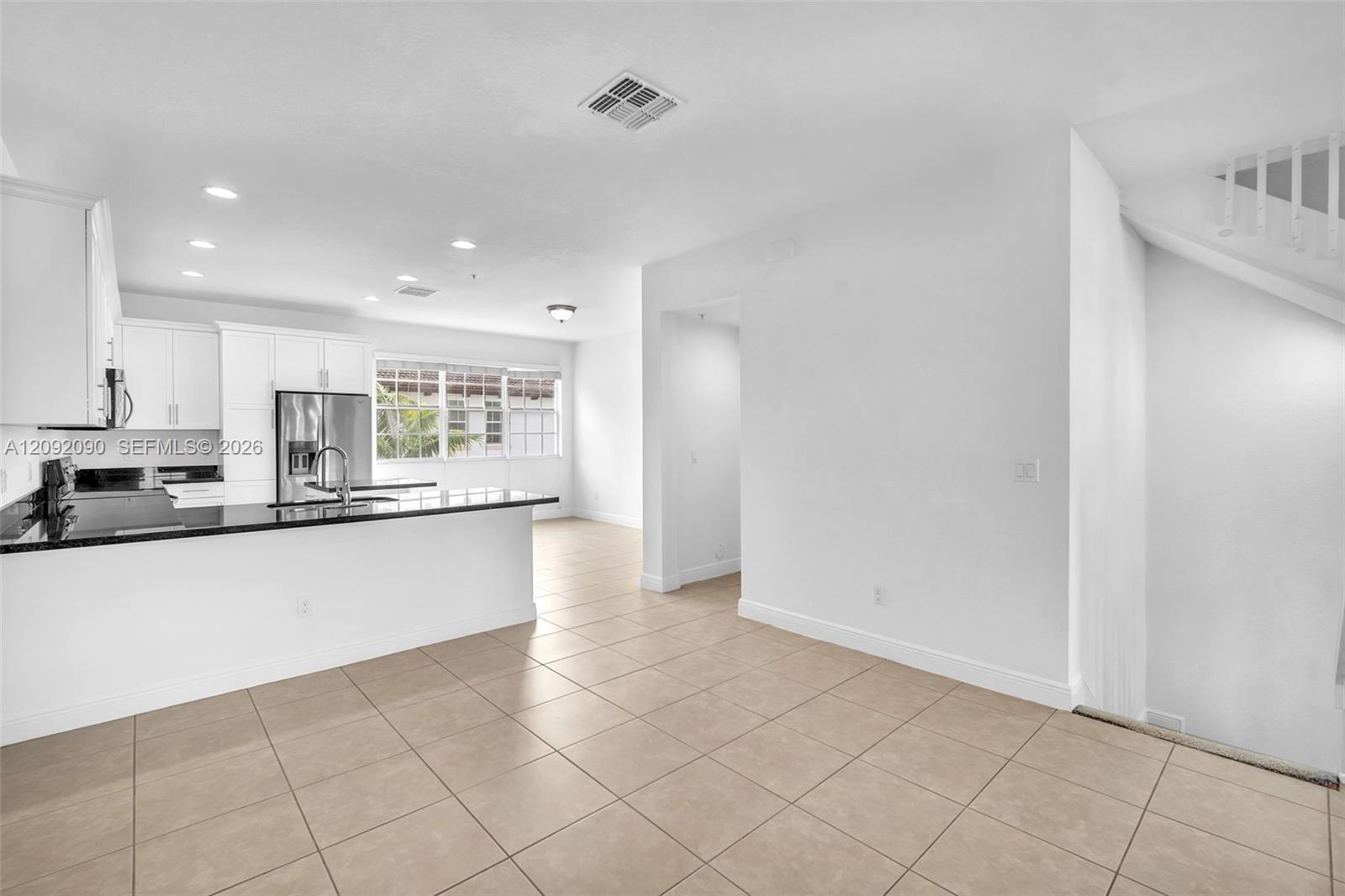 Kitchen featuring white shaker-style cabinetry, a stone countertop peninsula, stainless steel appliances, and tile flooring