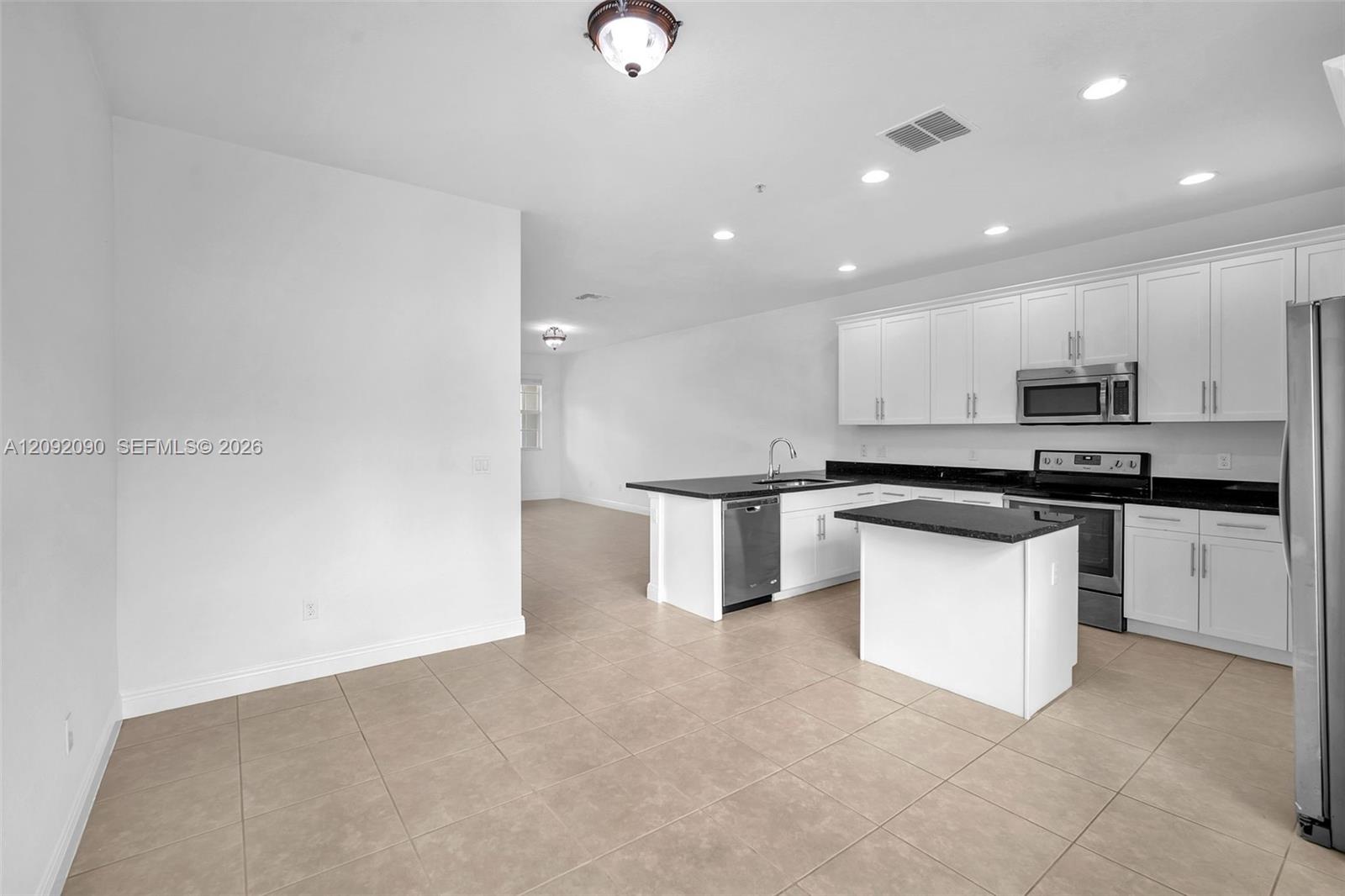 Kitchen featuring white cabinetry, dark countertops, an integrated island, stainless steel appliances, and tile flooring