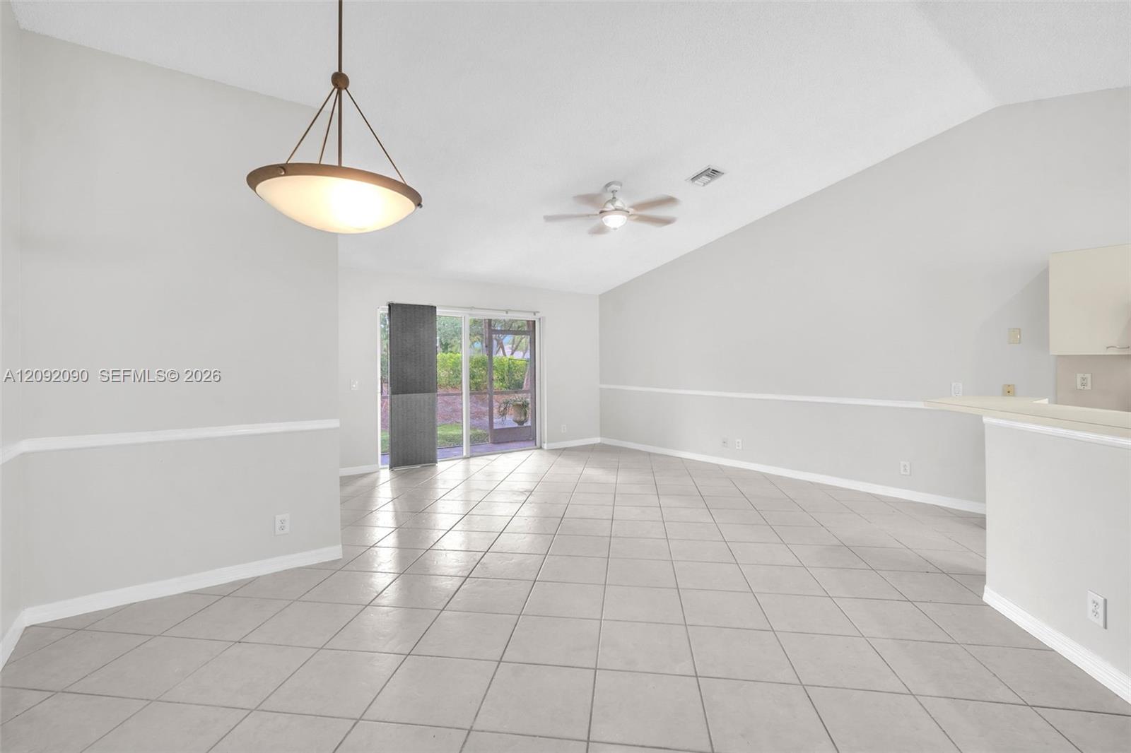 Open-concept interior featuring vaulted ceilings, ceramic tile flooring, a tiered pendant light fixture, a ceiling fan, and sliding glass doors