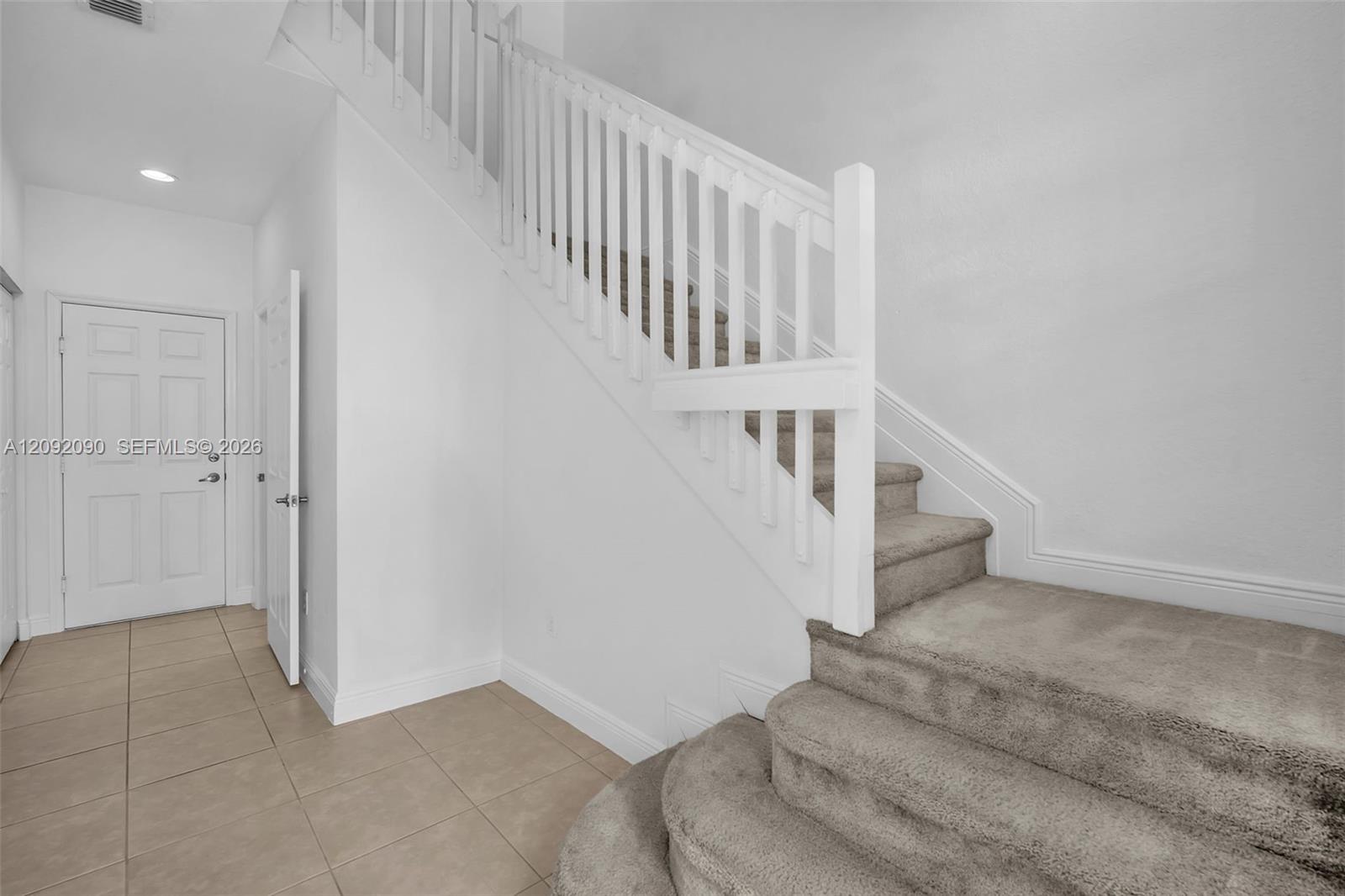 Interior foyer featuring large-format tile flooring, a recessed lighting fixture, and a staircase with carpeted treads and a painted white balustrade