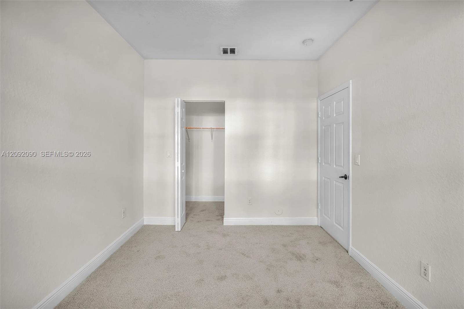 Neutral wall-to-wall carpeting, high ceilings, six-panel interior door, and walk-in closet with built-in shelving