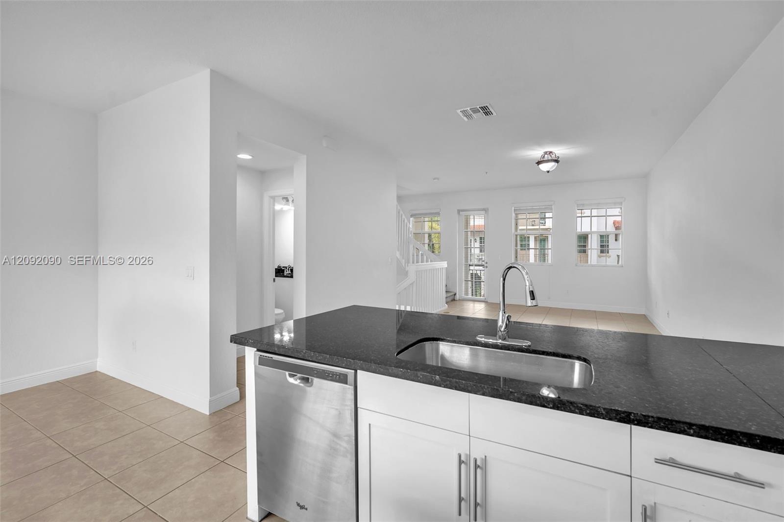 Kitchen featuring white cabinetry, dark stone-finish countertops, stainless steel undermount sink with gooseneck faucet, and stainless steel dishwasher