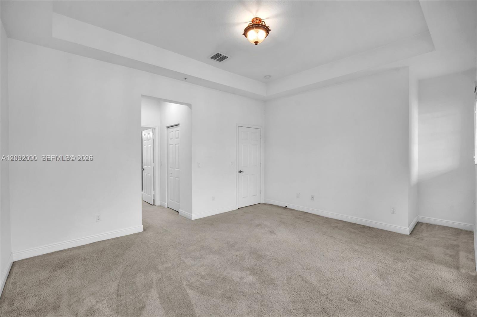 Room featuring a tray ceiling, neutral carpeting, and a central flush-mount light fixture