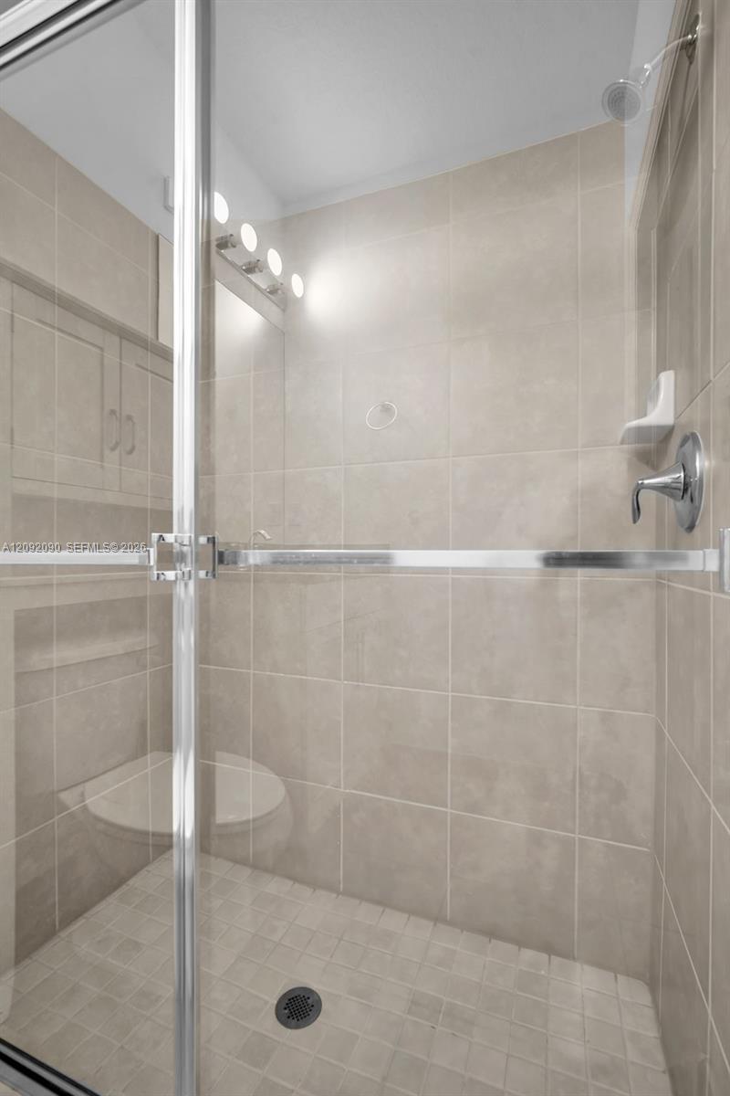 Walk-in shower featuring floor-to-ceiling neutral tile, glass enclosure with chrome hardware, built-in recessed shelf, and fixed shower head