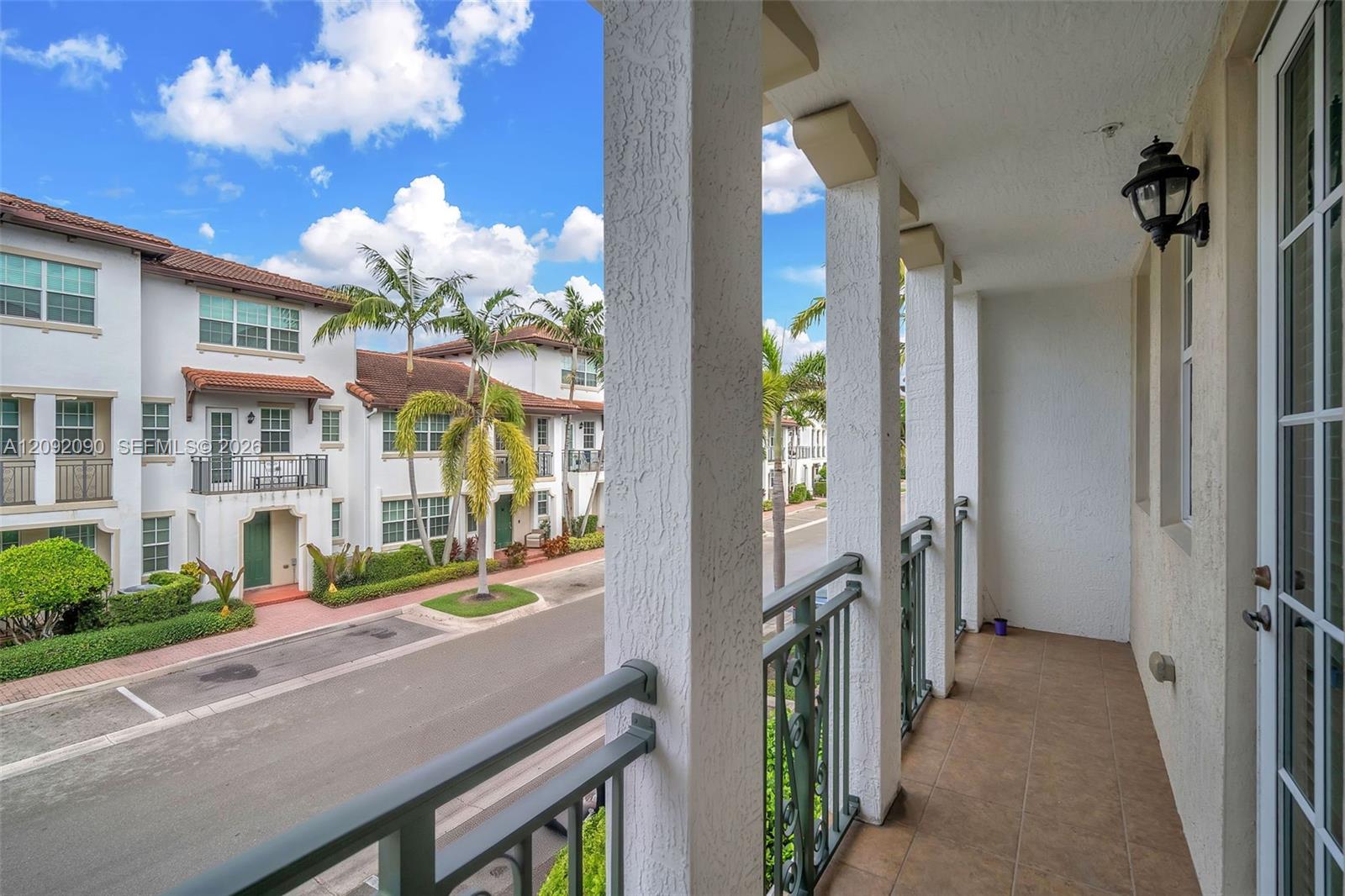 Covered balcony featuring tile flooring, structural stucco columns, dark metal railings, and a wall-mounted exterior light fixture