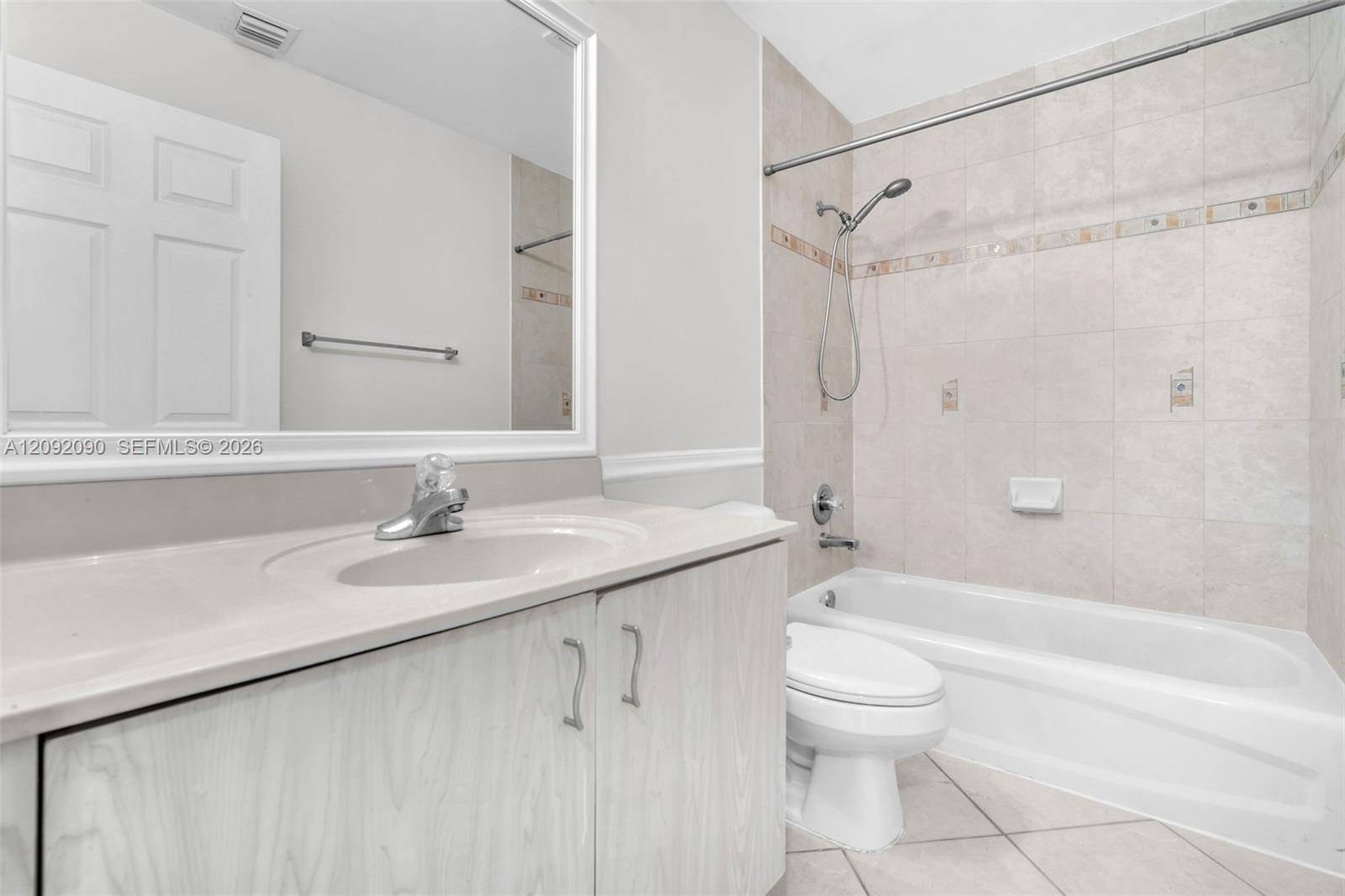 Bathroom featuring a vanity with an integrated countertop, large framed wall mirror, light-toned cabinetry, ceramic tile flooring, and a tub-shower combination with tiled surround