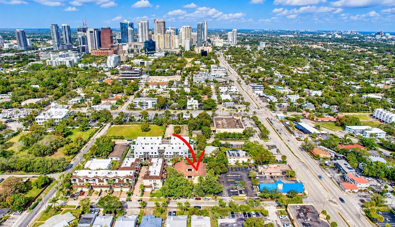 Aerial perspective featuring an urban lot with mature trees and a multi-unit building, situated within a metropolitan area