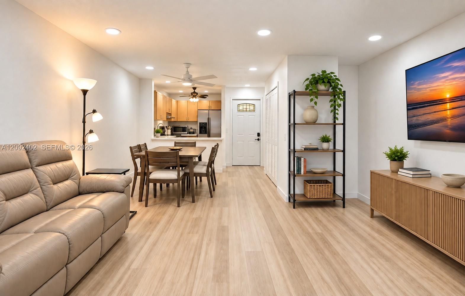 TV console & plants virtually staged for illustrative purposes. Open-concept interior featuring light wood-finish flooring, recessed lighting, white cabinetry, and an exterior entry door with an arched glass inset