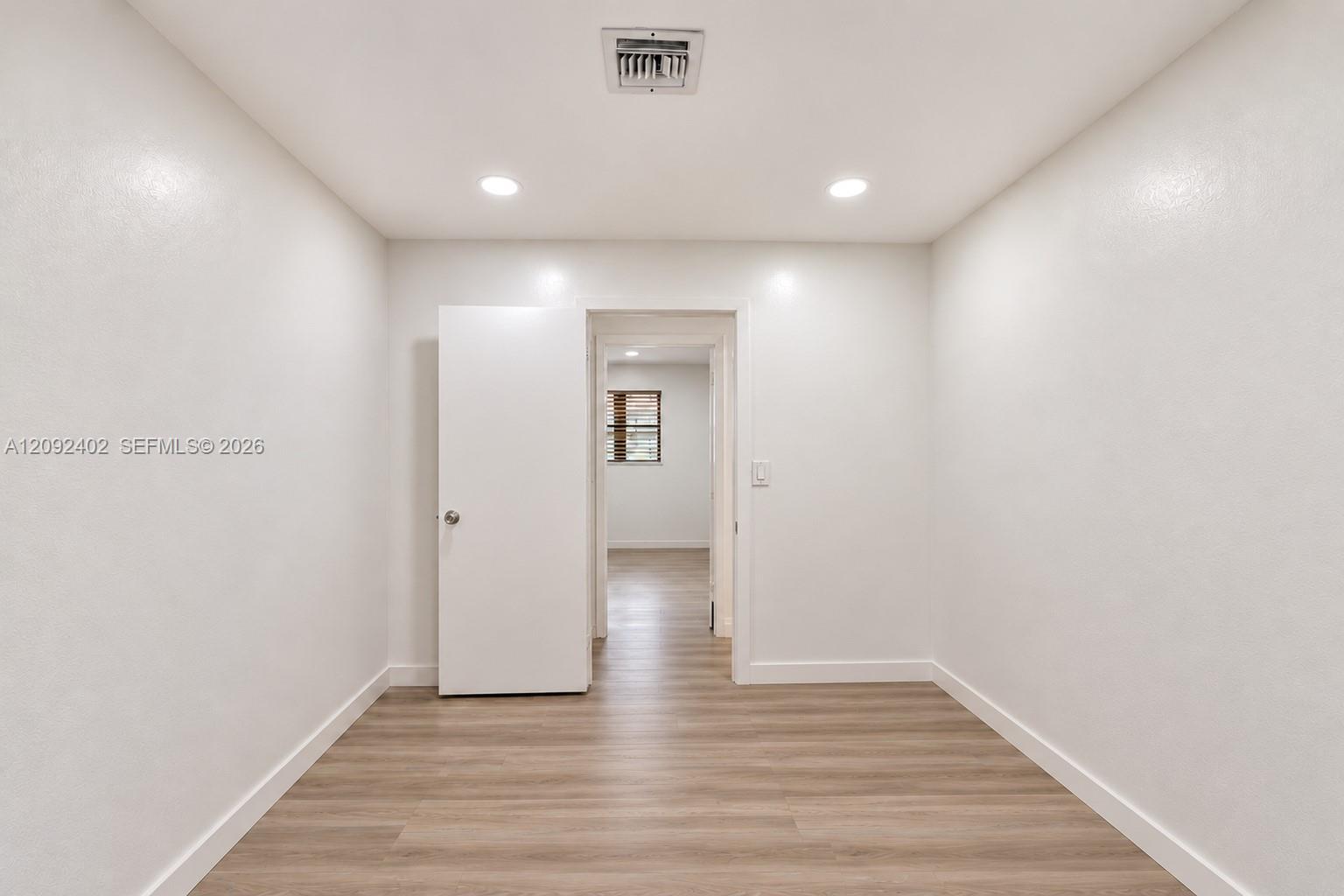 Interior space featuring light-toned wood-finish flooring, crisp neutral wall paint, recessed lighting, and a solid-core interior door