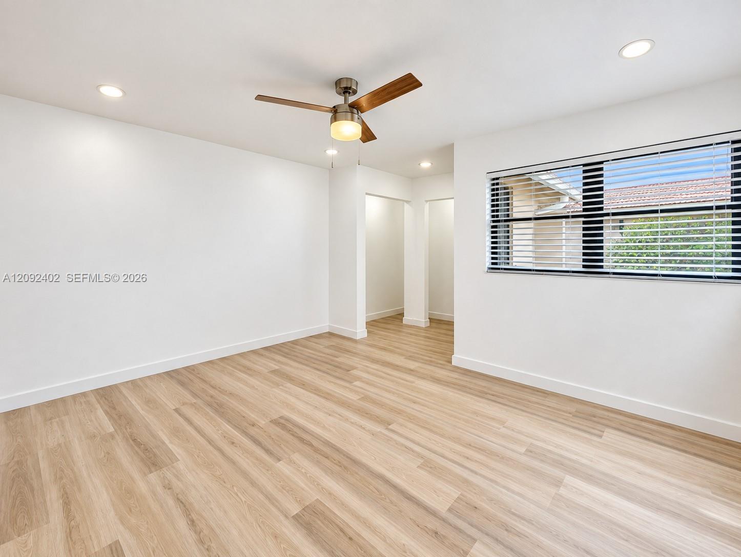 Neutral interior space featuring wood-finish flooring, recessed lighting, a modern ceiling fan with light fixture, and large windows with horizontal blinds