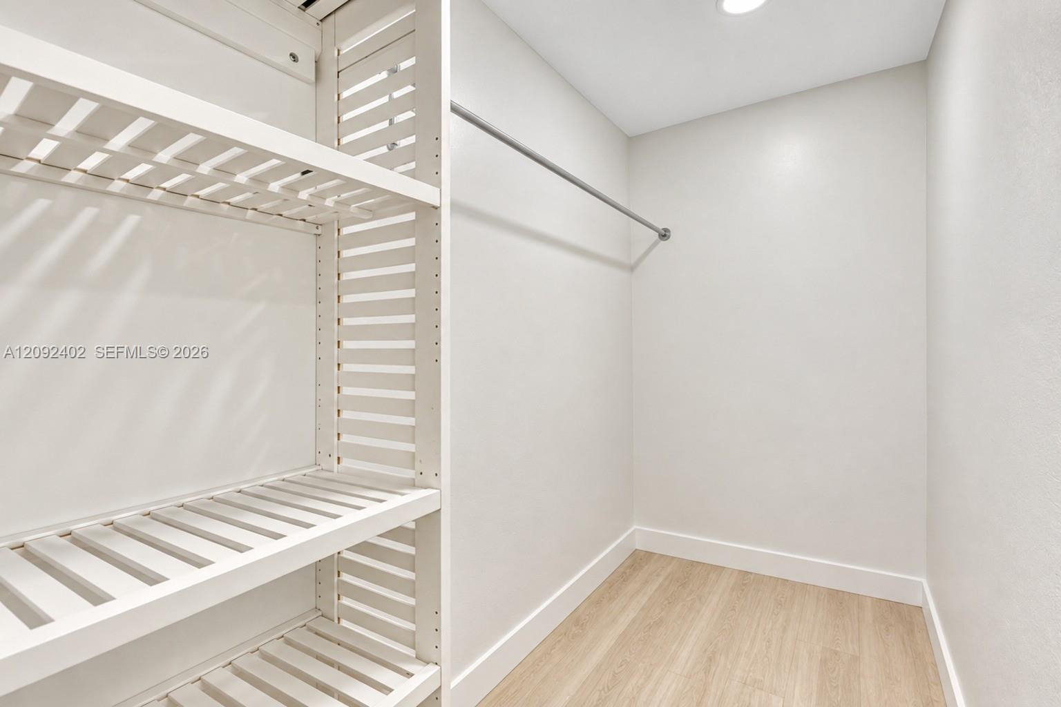 Walk-in closet featuring white slatted built-in shelving, a metal hanging rod, and wood-finish flooring