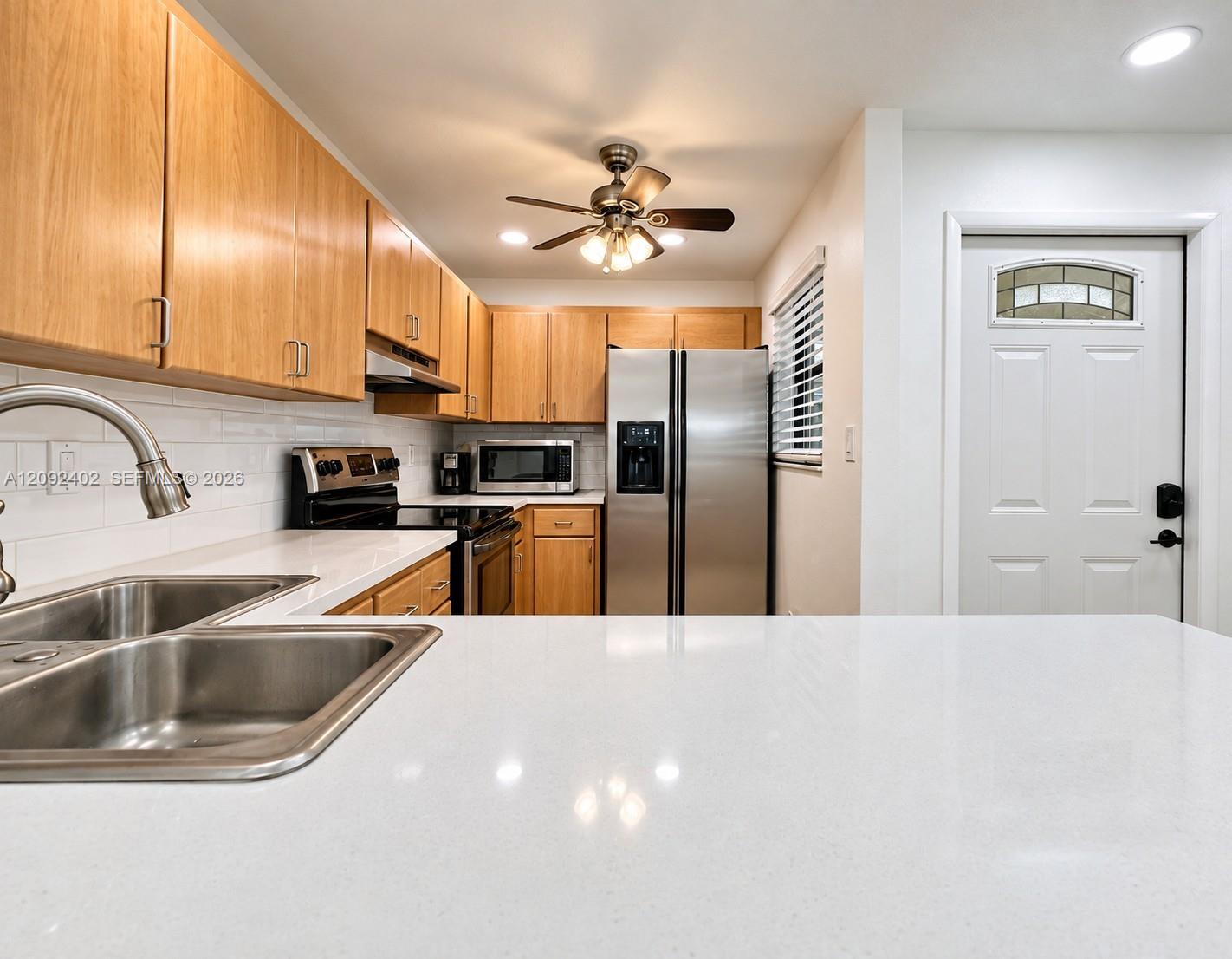 Kitchen featuring light-finish cabinetry, white solid-surface countertops, subway tile backsplash, stainless steel appliances, and a double-basin stainless steel sink