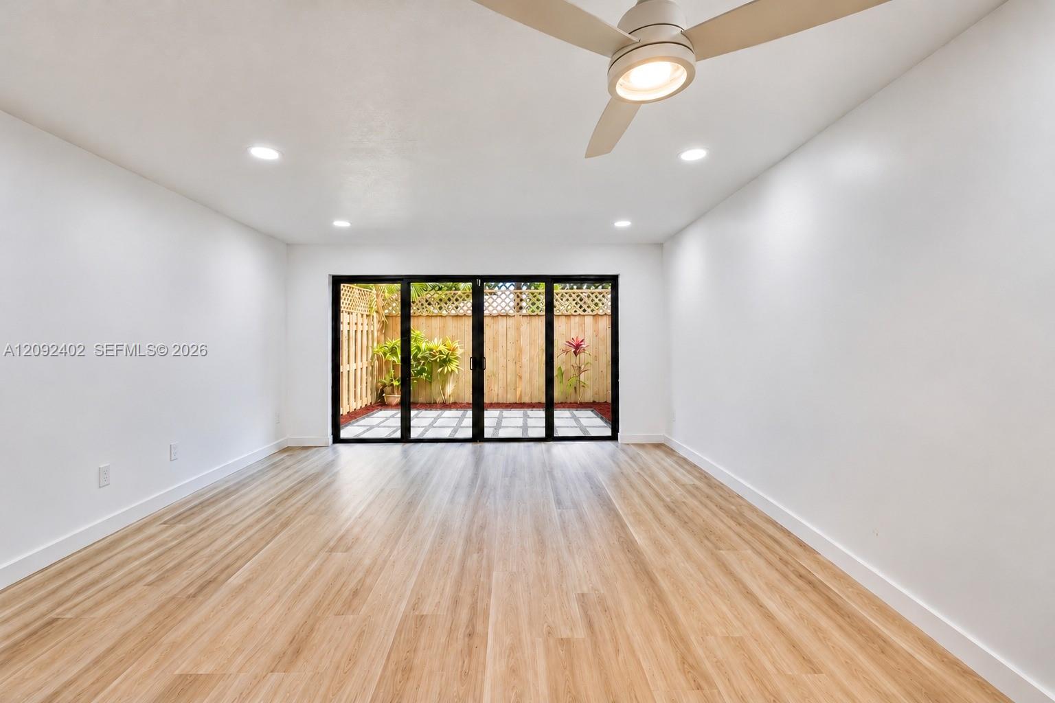 Interior space featuring wood-finish flooring, recessed lighting, and a modern ceiling fan, highlighted by a multi-panel glass door system opening to a private patio with wood fencing