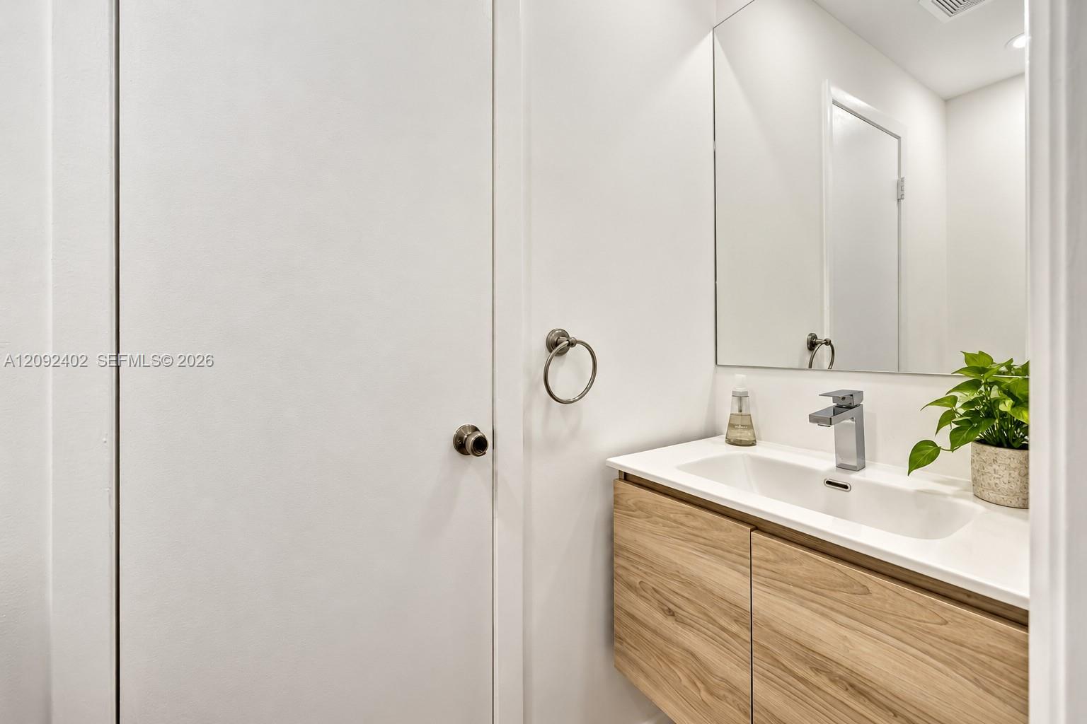 Floating vanity with wood-finish cabinetry, white countertop, integrated rectangular sink, chrome single-handle faucet, and wall-mounted mirror