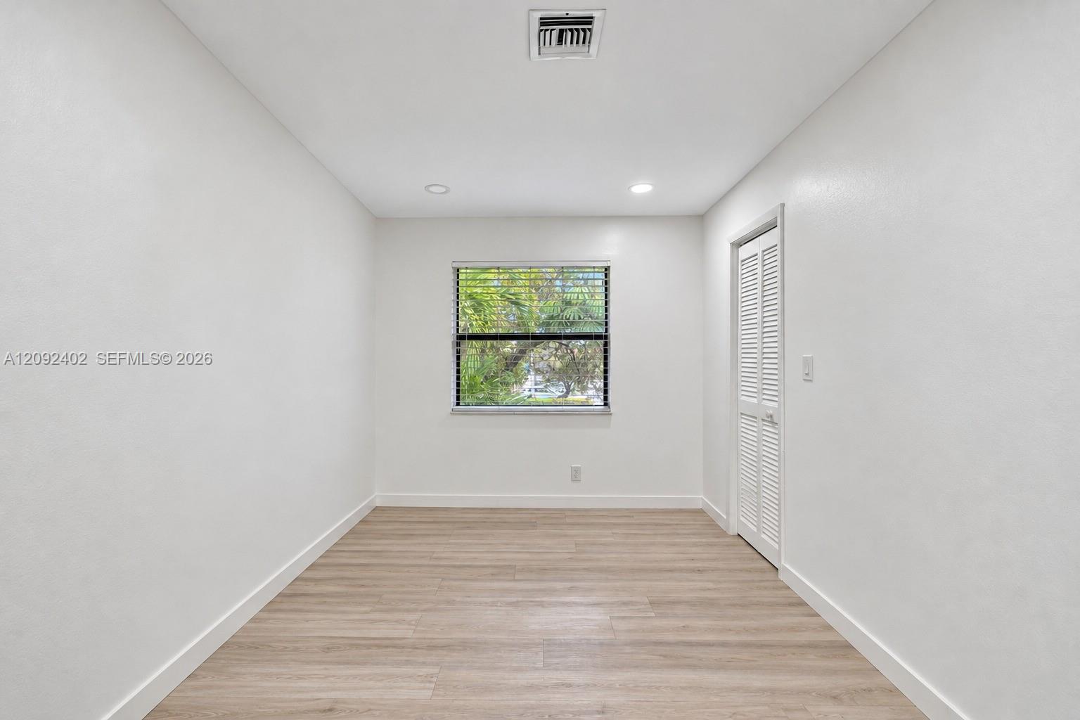 Neutral-toned room featuring wood-finish flooring, recessed lighting, and a window with horizontal blinds, complemented by a white louvered closet door