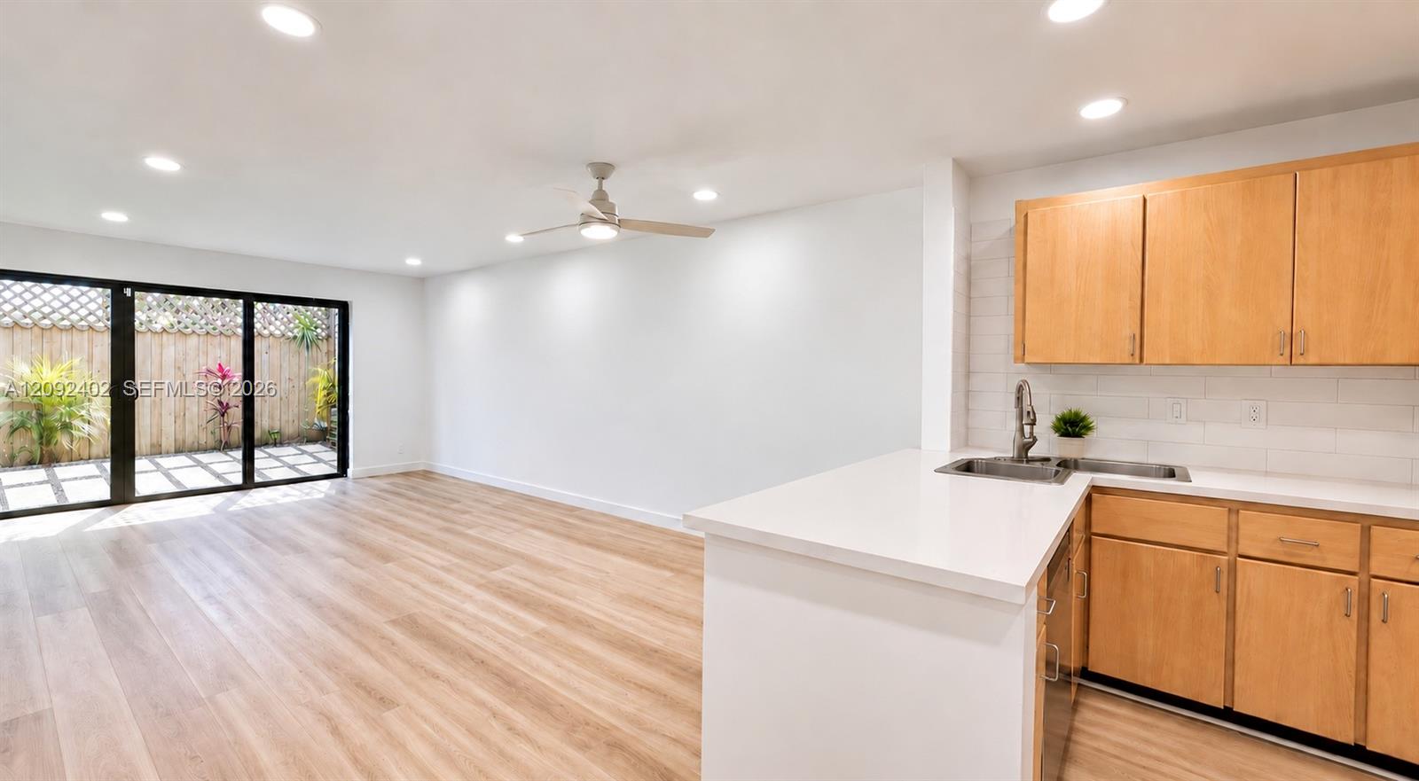 Kitchen featuring wood-finish cabinetry, white countertops, and subway tile backsplash, complemented by wood-finish flooring, recessed lighting, and sliding glass doors